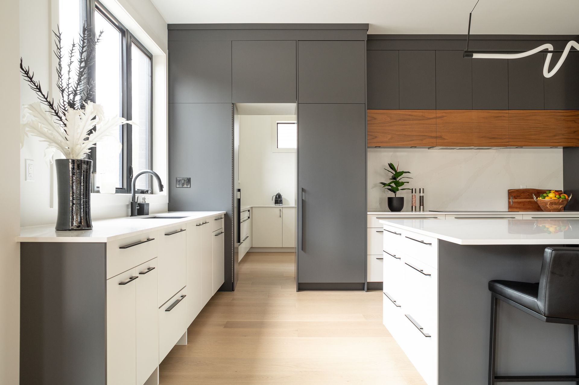 Modern kitchen with gray and white cabinetry, light wood floors, and island.