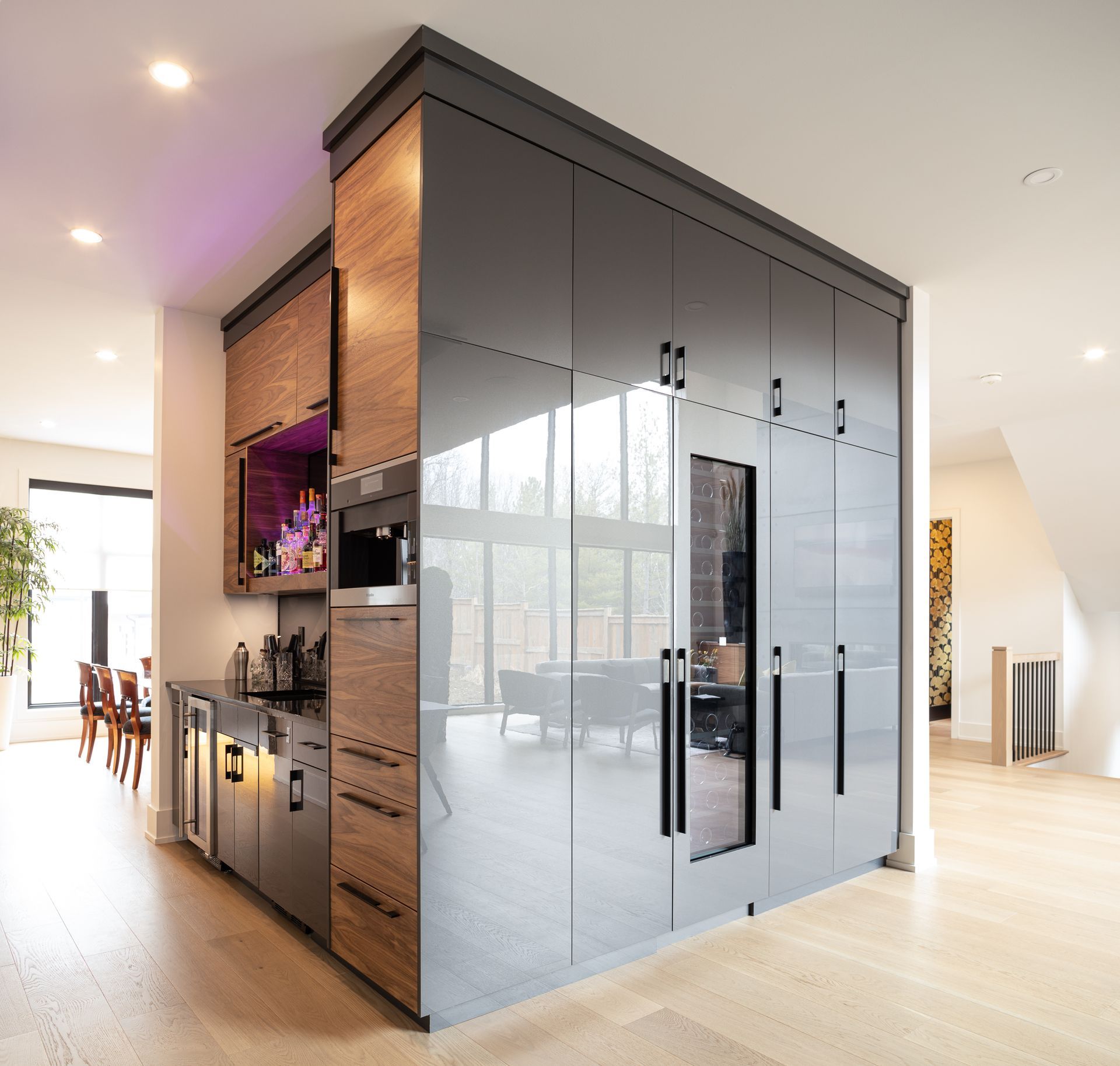 Modern built-in bar with gray cabinetry, wood accents, and a wine fridge, separating two living areas.
