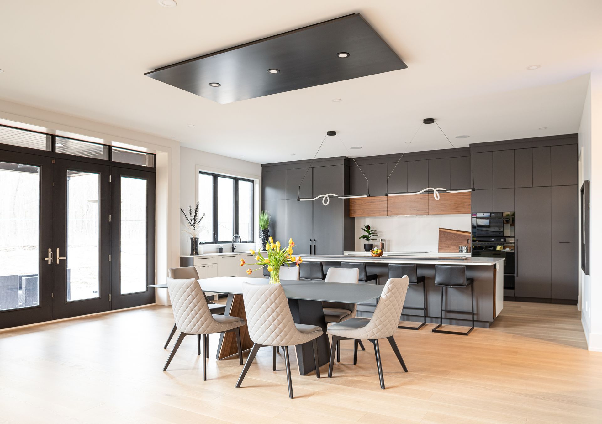 Modern kitchen and dining room with dark cabinetry, gray island, and light wood flooring.
