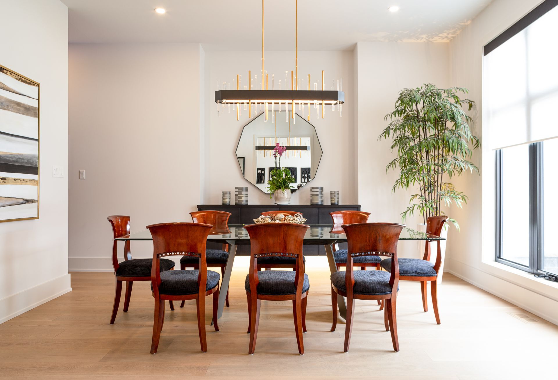 Elegant dining room with a table, chairs, large mirror, and plant. Light wood floors and neutral walls.