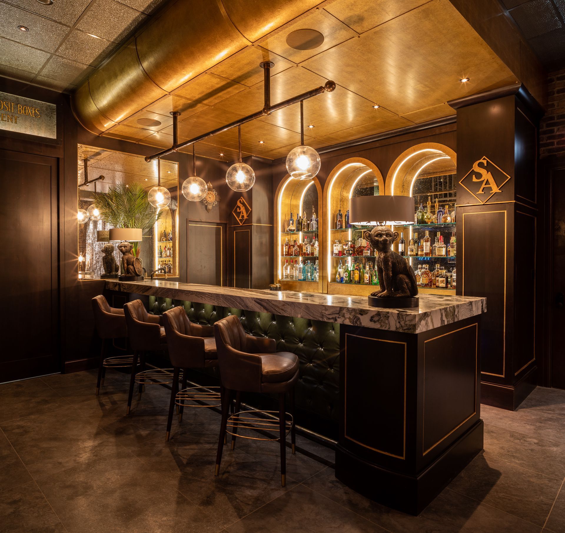 Luxurious bar with marble countertop, tufted green backing, and globe pendant lights. Gold accents and dark wood create a moody atmosphere.