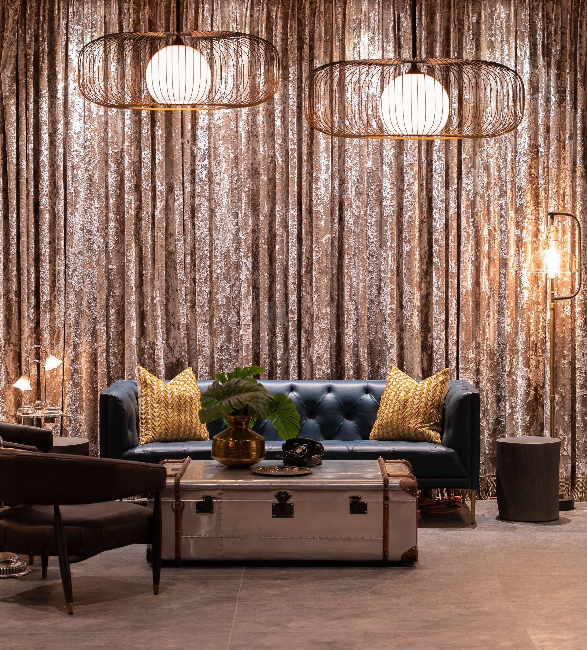 Living room with blue sofa, gold pillows, coffee table, and bronze light fixtures against draped fabric backdrop.