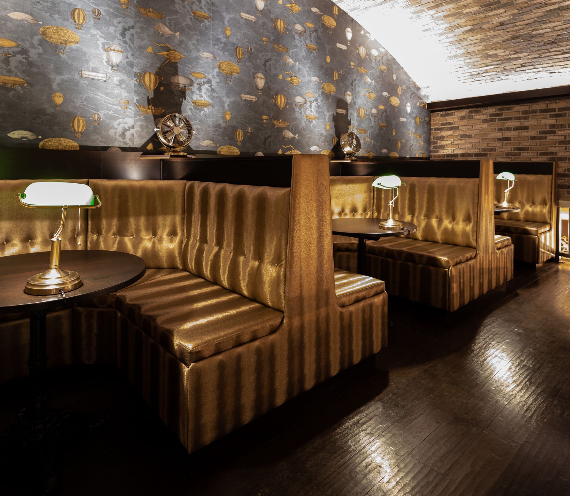 Booth seating in a dimly lit restaurant, gold upholstery, dark wood floors, and patterned wallpaper.