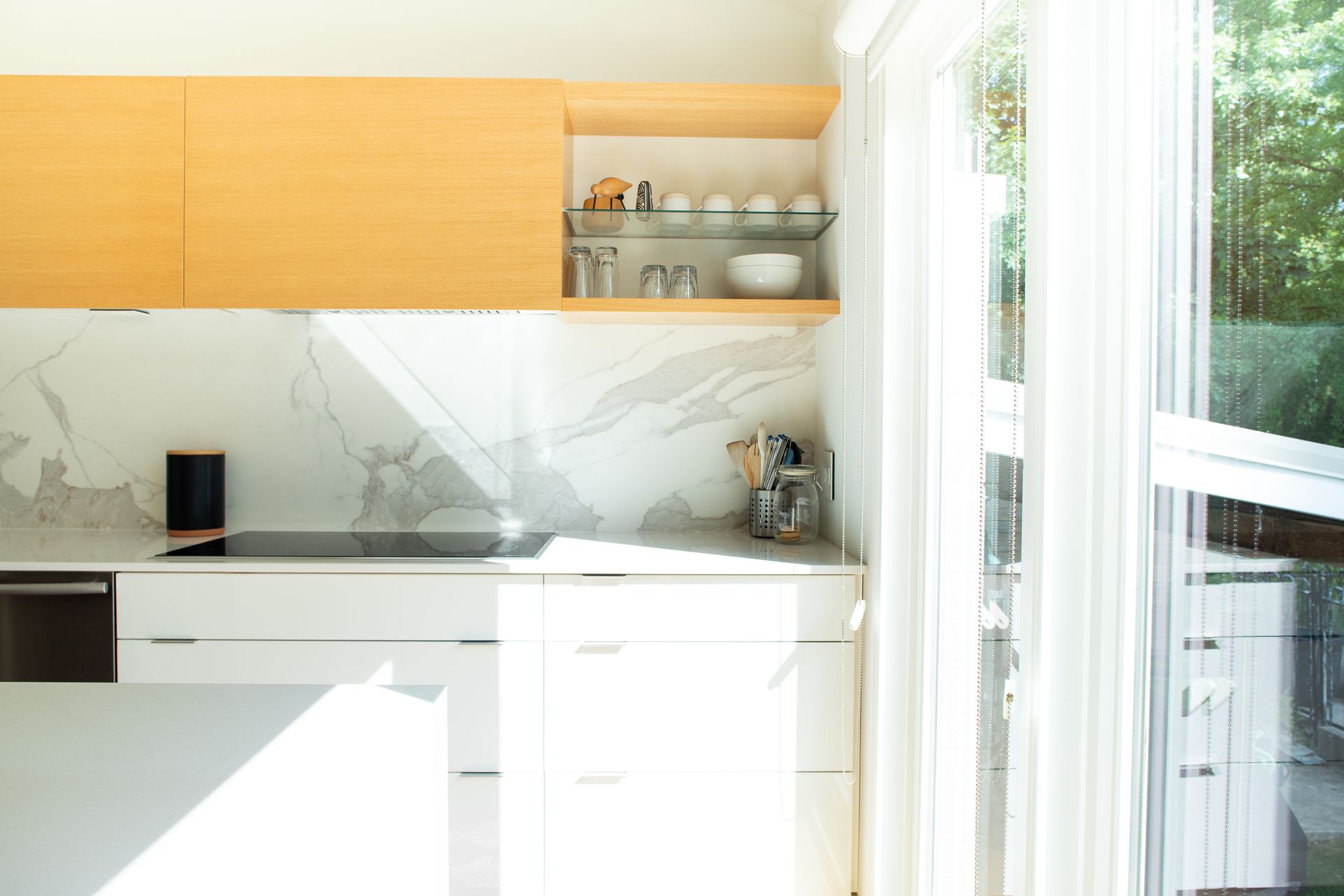 Modern kitchen with light wood cabinets, white countertops, and a large window.
