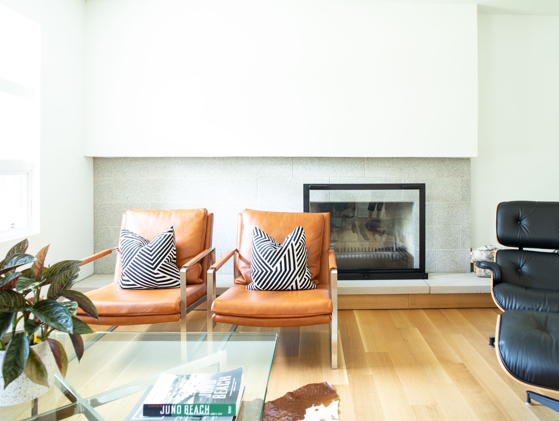 Two tan leather chairs with black and white pillows face a fireplace.