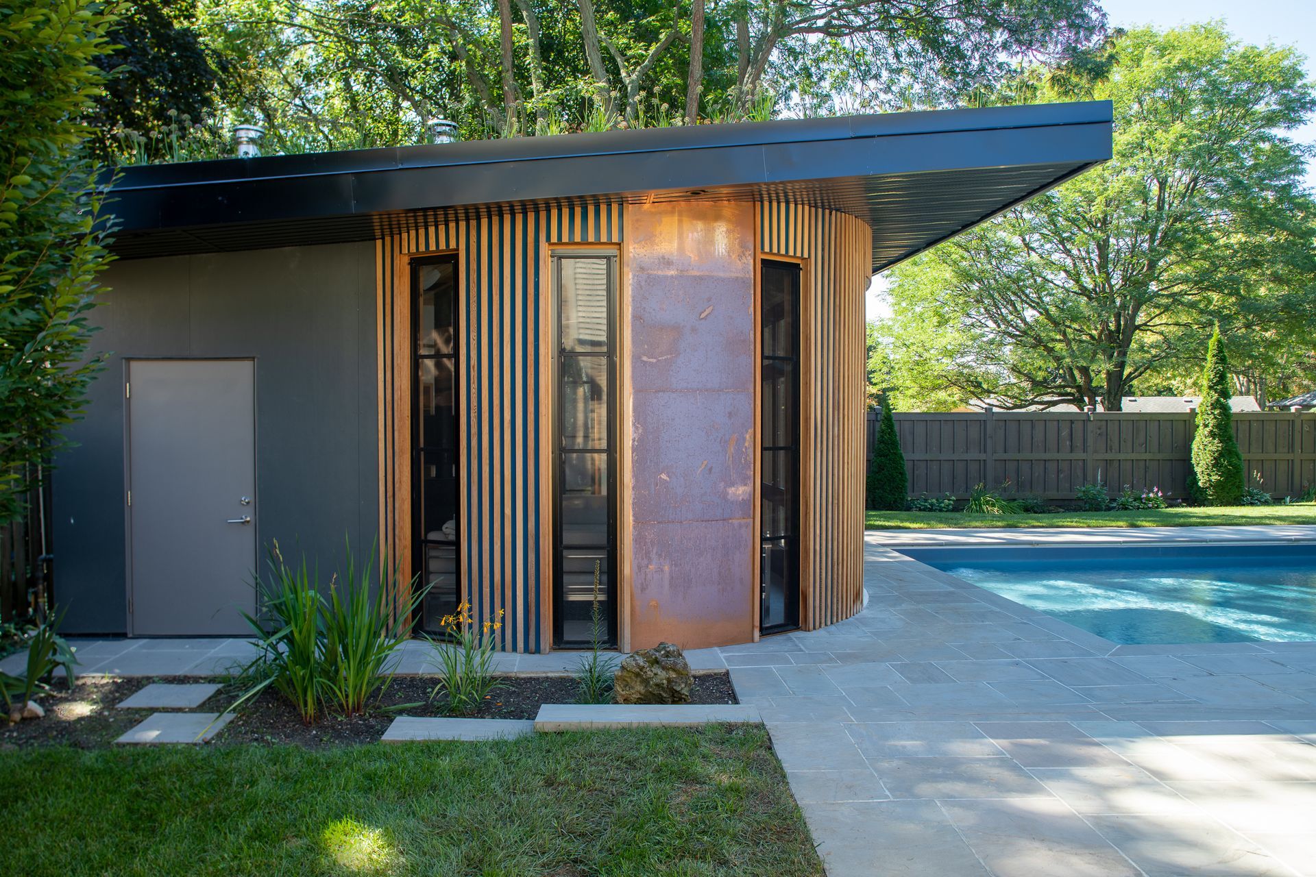 Modern pool house with grey and wood exterior, next to a pool.