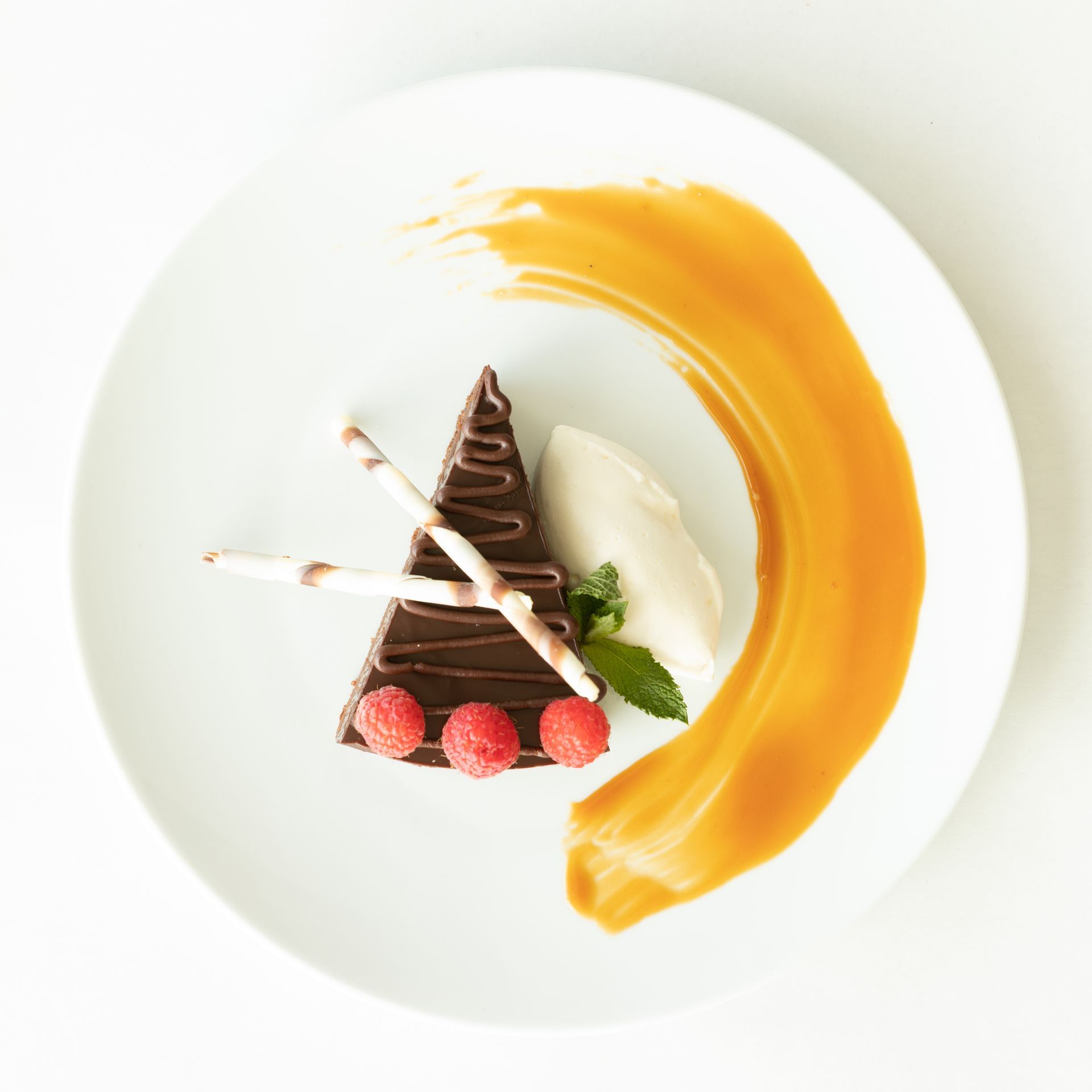 Chocolate dessert with caramel sauce and raspberries on a white plate.