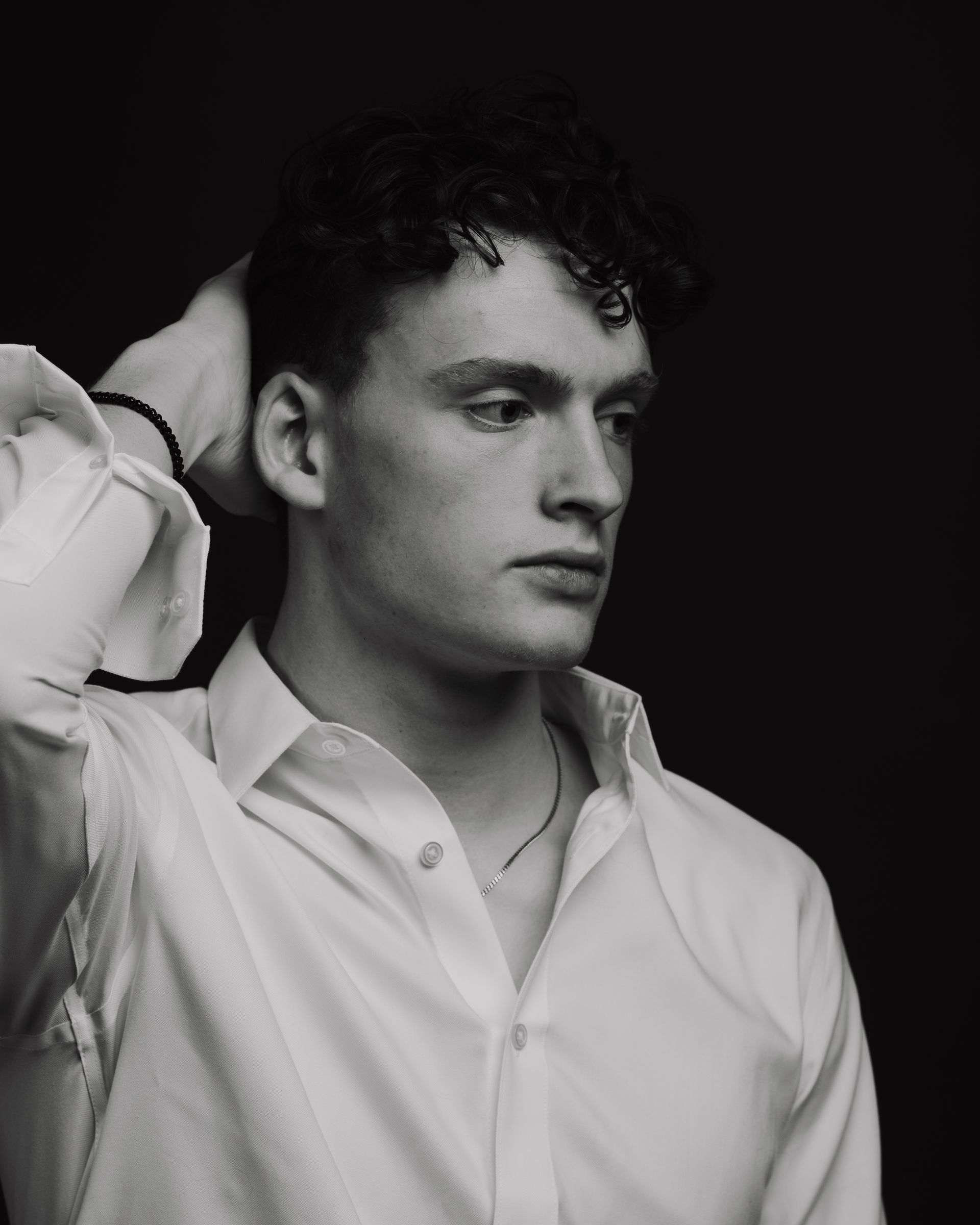 Man in white shirt with hand in hair, looking down, black and white.