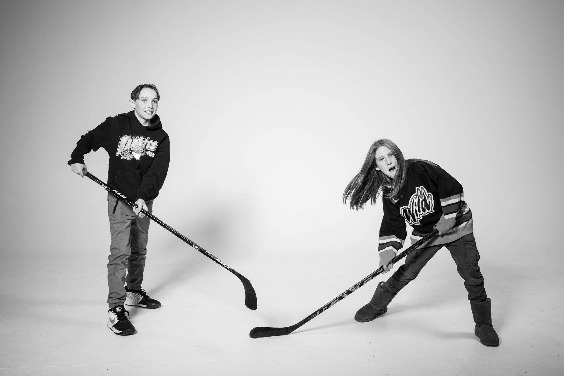 Two people posing with hockey sticks against a white backdrop.