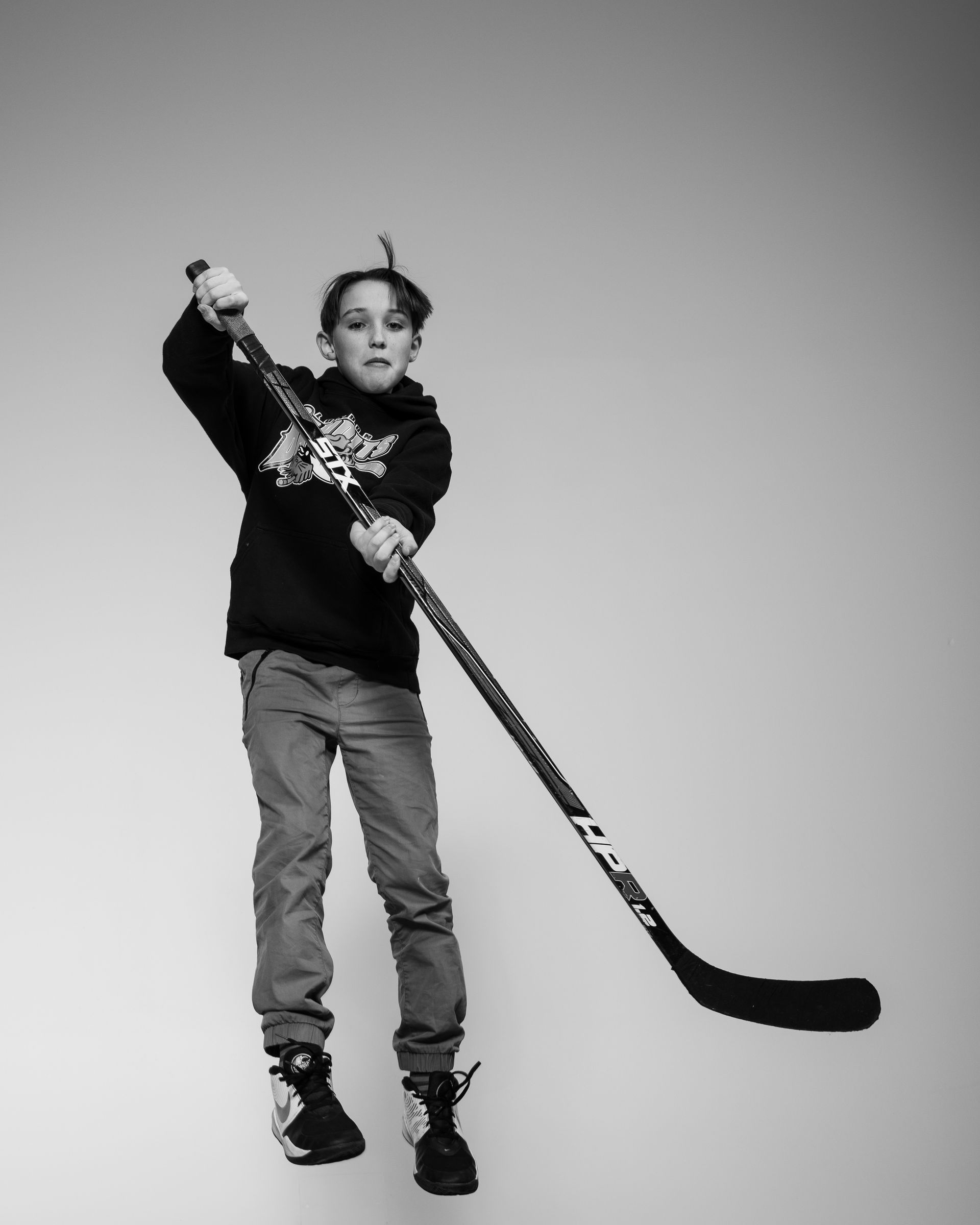 Boy jumping with hockey stick, indoors, black and white.