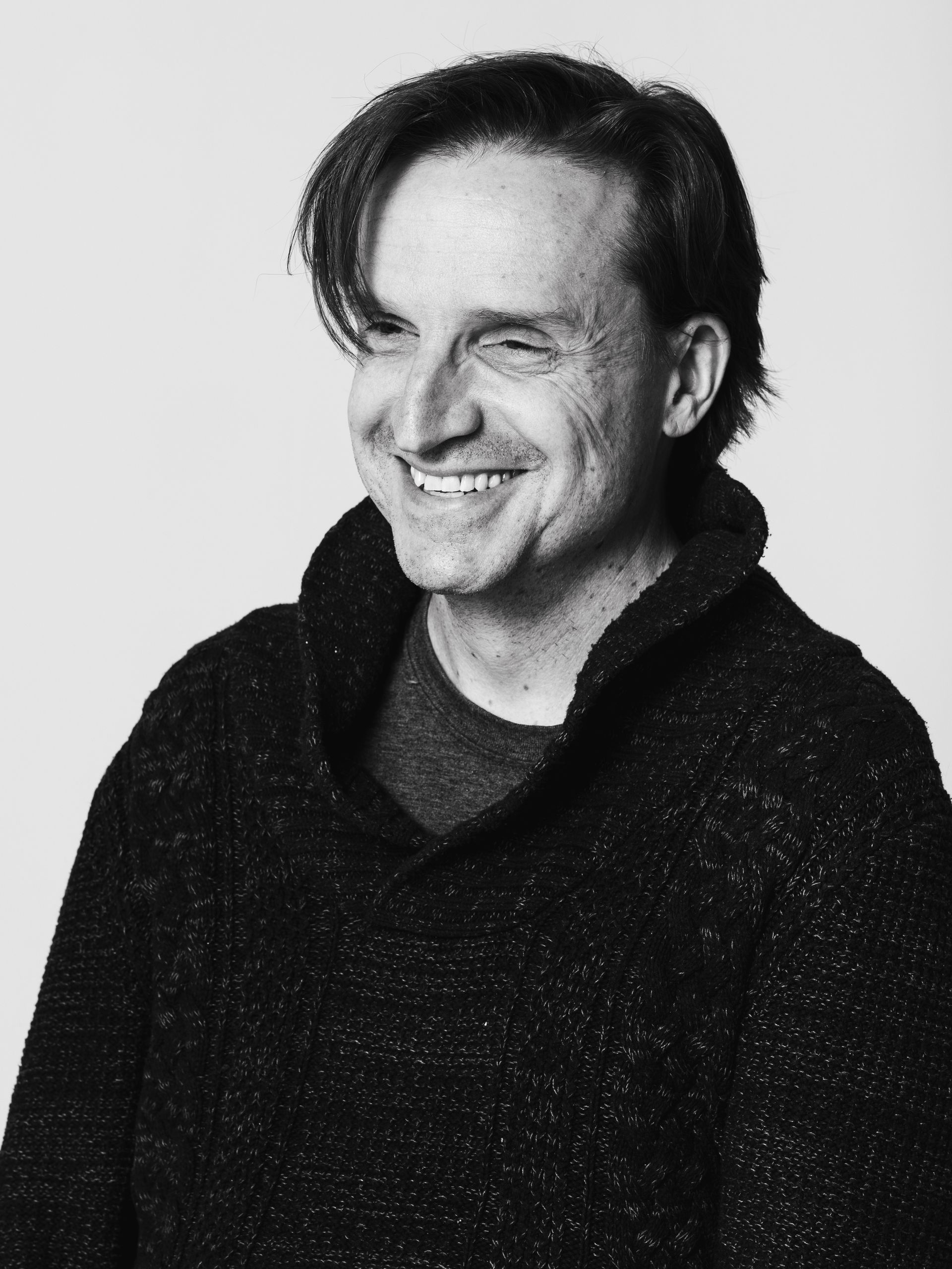 Man smiling, wearing a dark sweater against a light background.