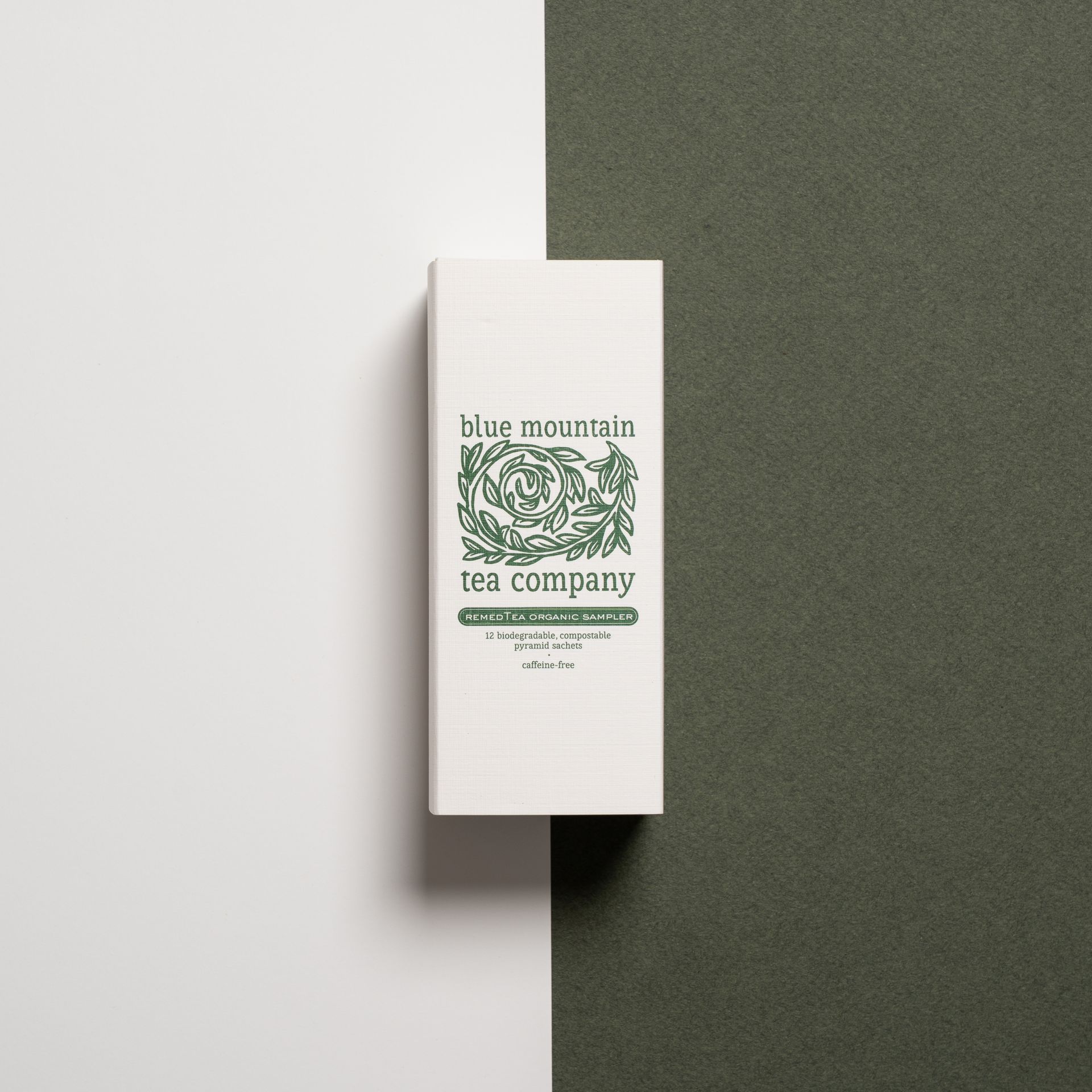 White tea box with green logo, centered on a white and dark green backdrop. 