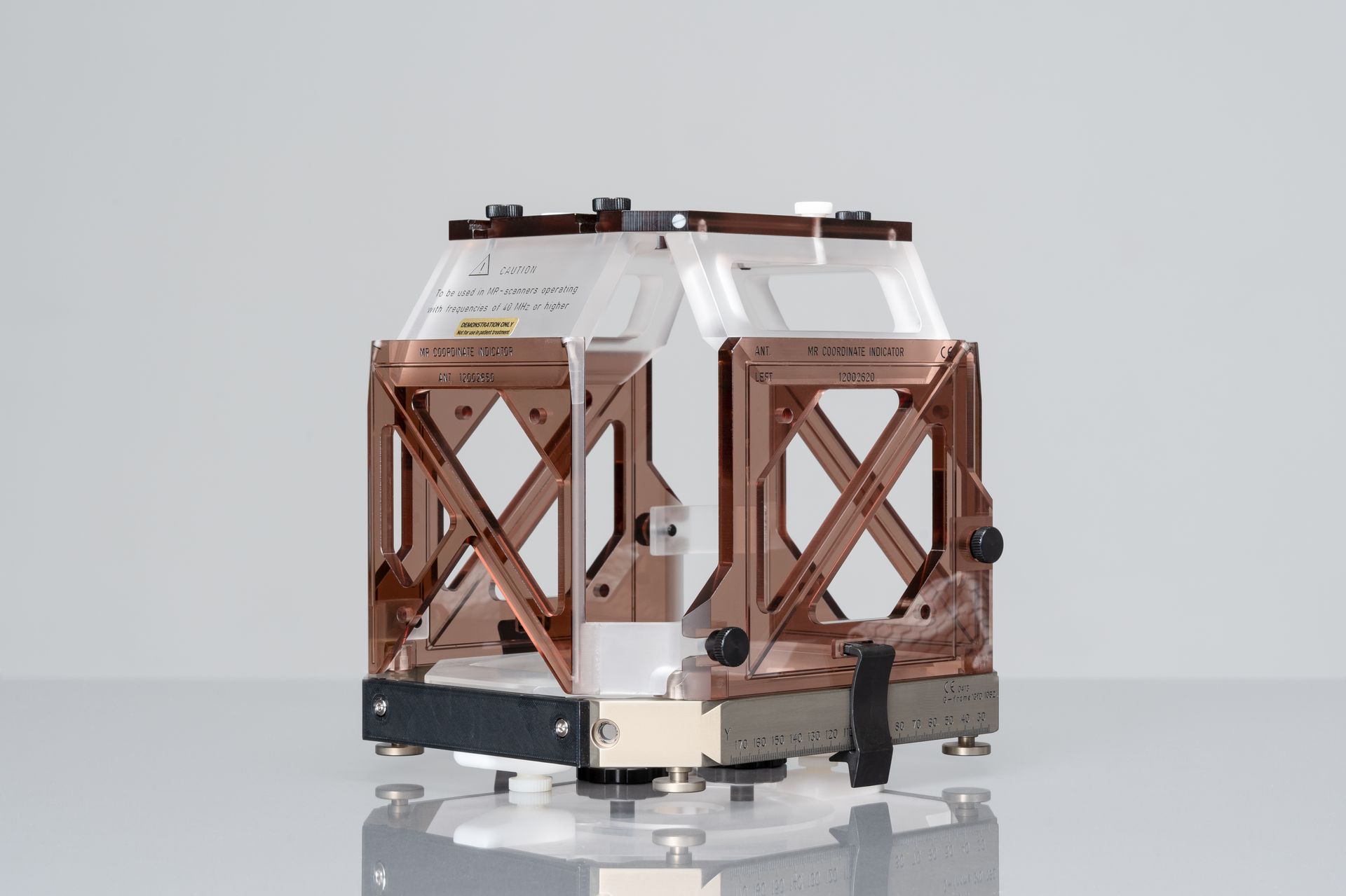Copper-colored framework and clear acrylic box structure, likely an instrument, on a reflective surface.