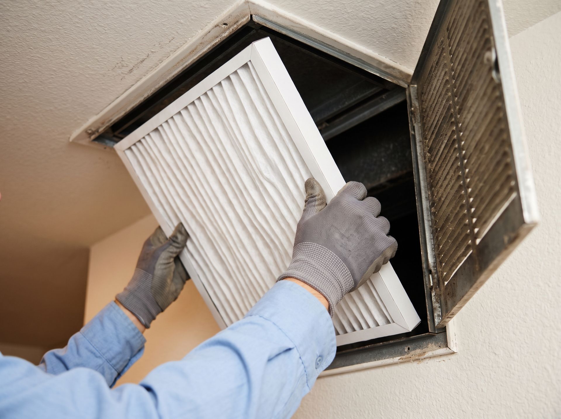 Gloved hands replacing a dirty HVAC air filter in a ceiling vent
