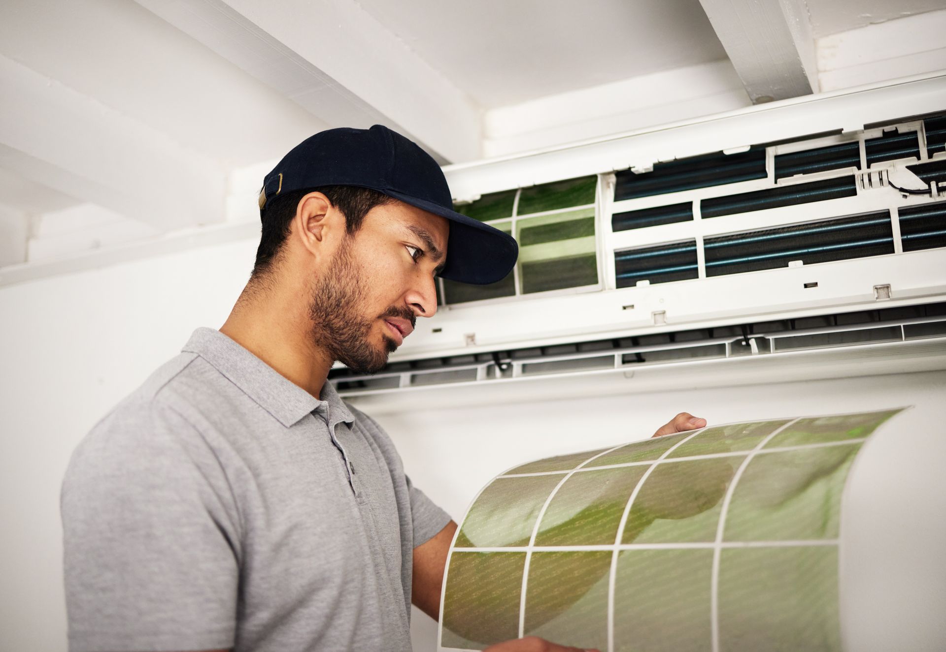 Man in a gray shirt and cap inspecting a green air filter indoors