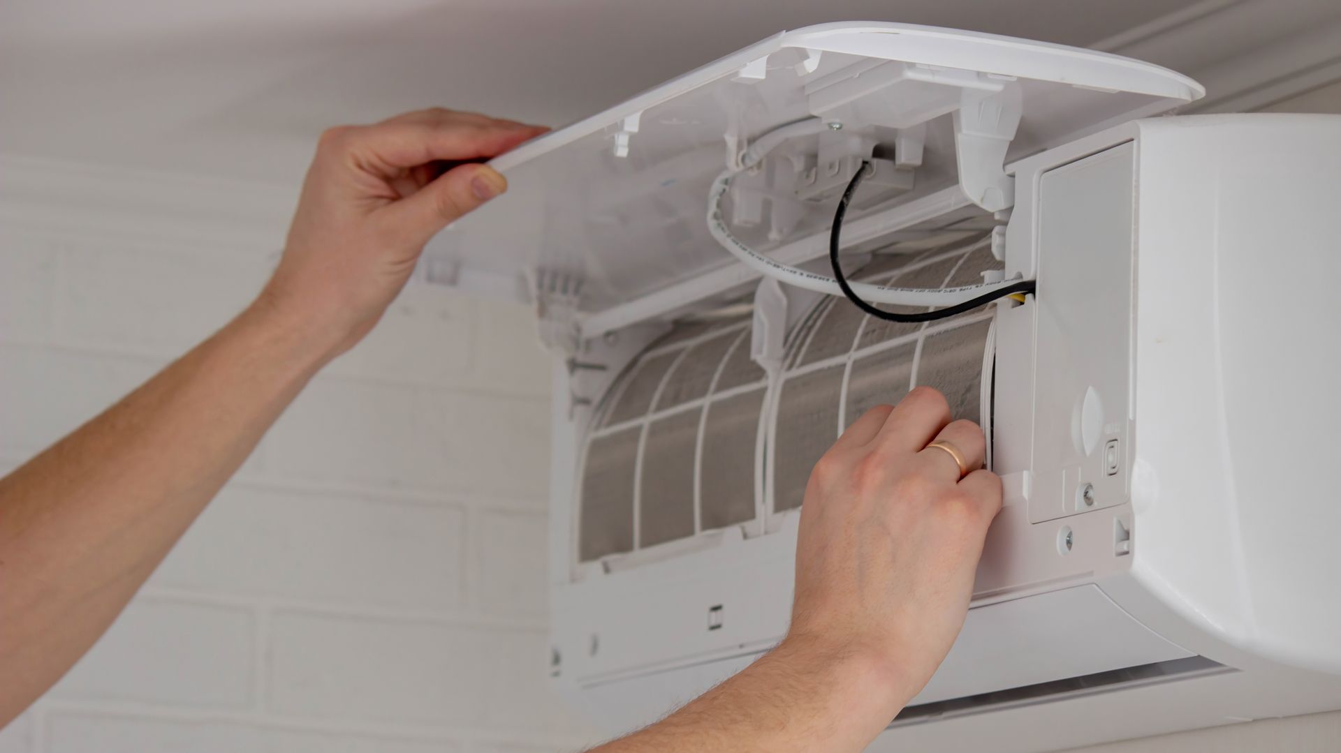 Hands adjust wiring inside a white wall-mounted air conditioner with the cover open.