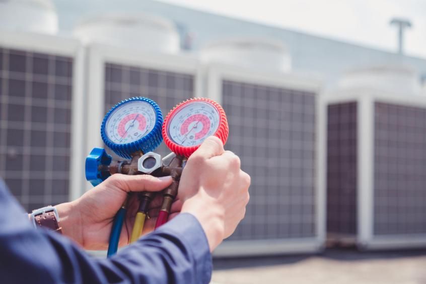 Technician holding HVAC pressure gauges in front of rooftop air conditioning units