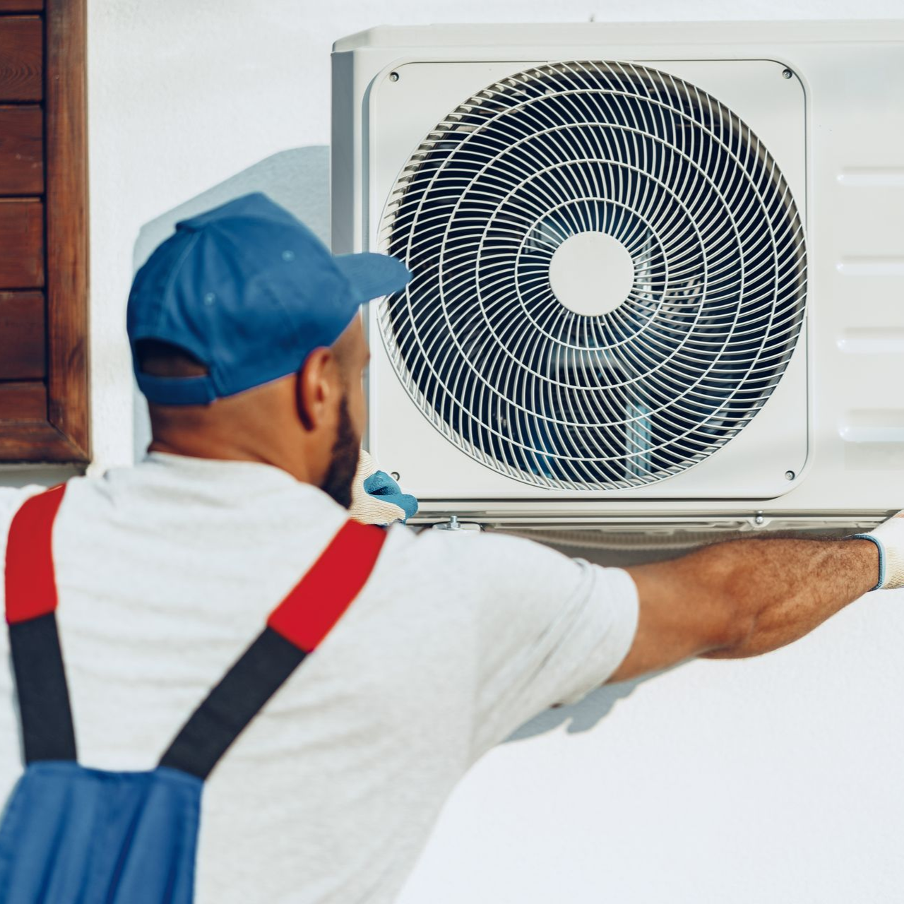 Technician installing a white outdoor air conditioner unit on a wall