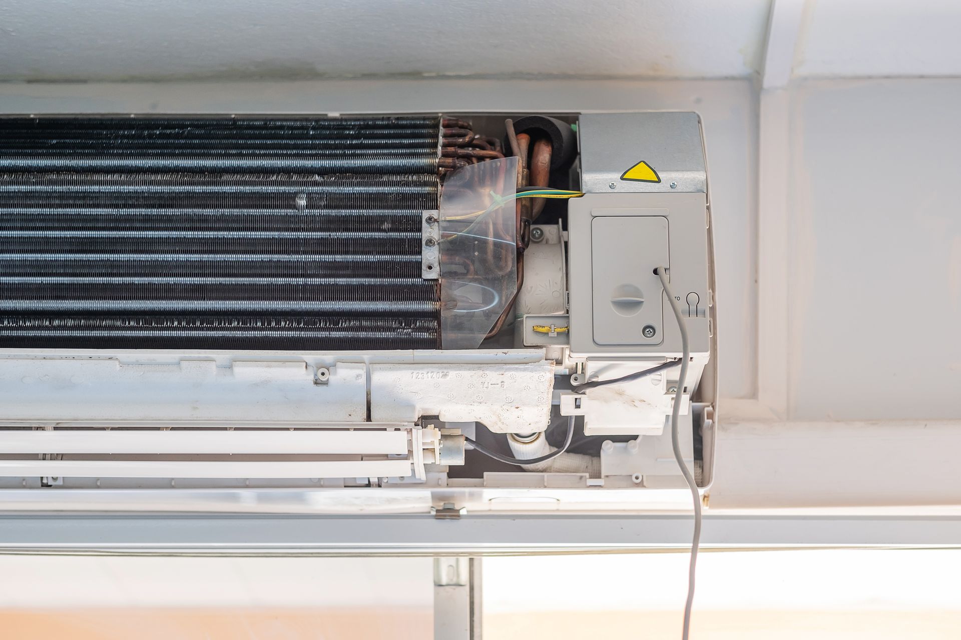 Open wall-mounted air conditioner with exposed wiring and control box under a white ceiling.