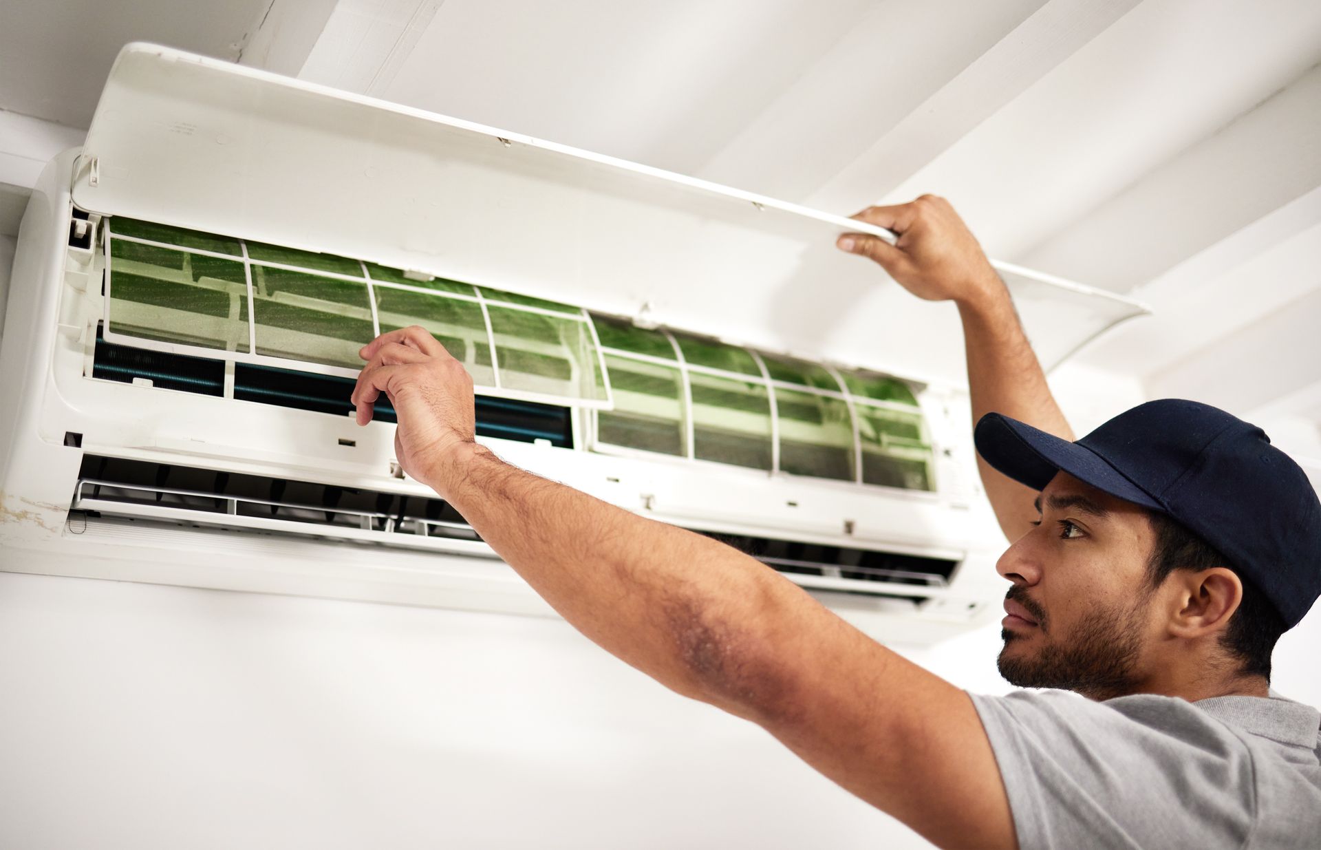 Technician cleaning a wall-mounted air conditioner filter indoors
