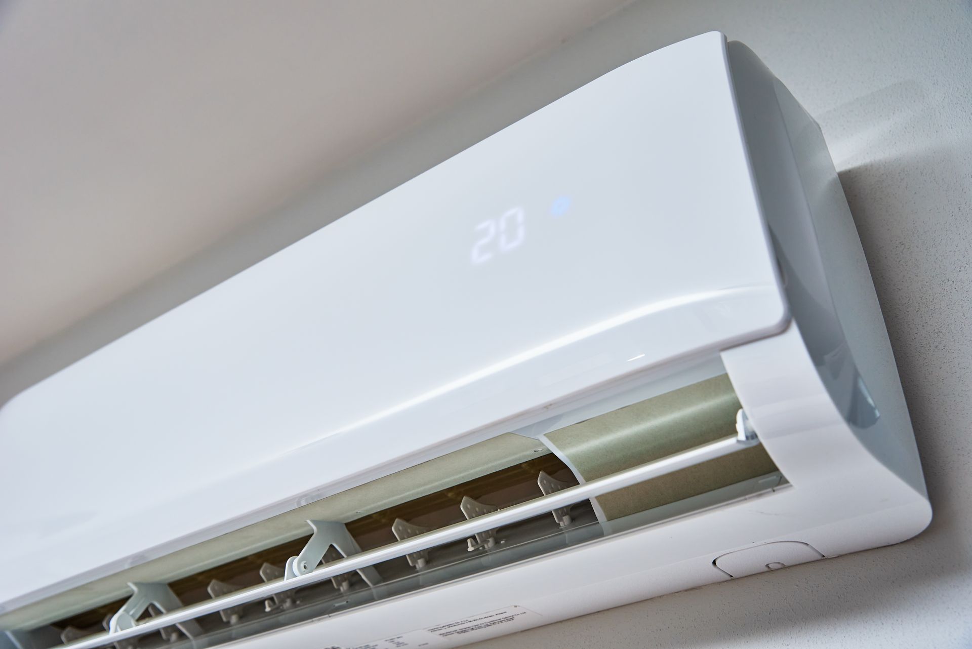White wall-mounted air conditioner with open front panel, angled near the ceiling.