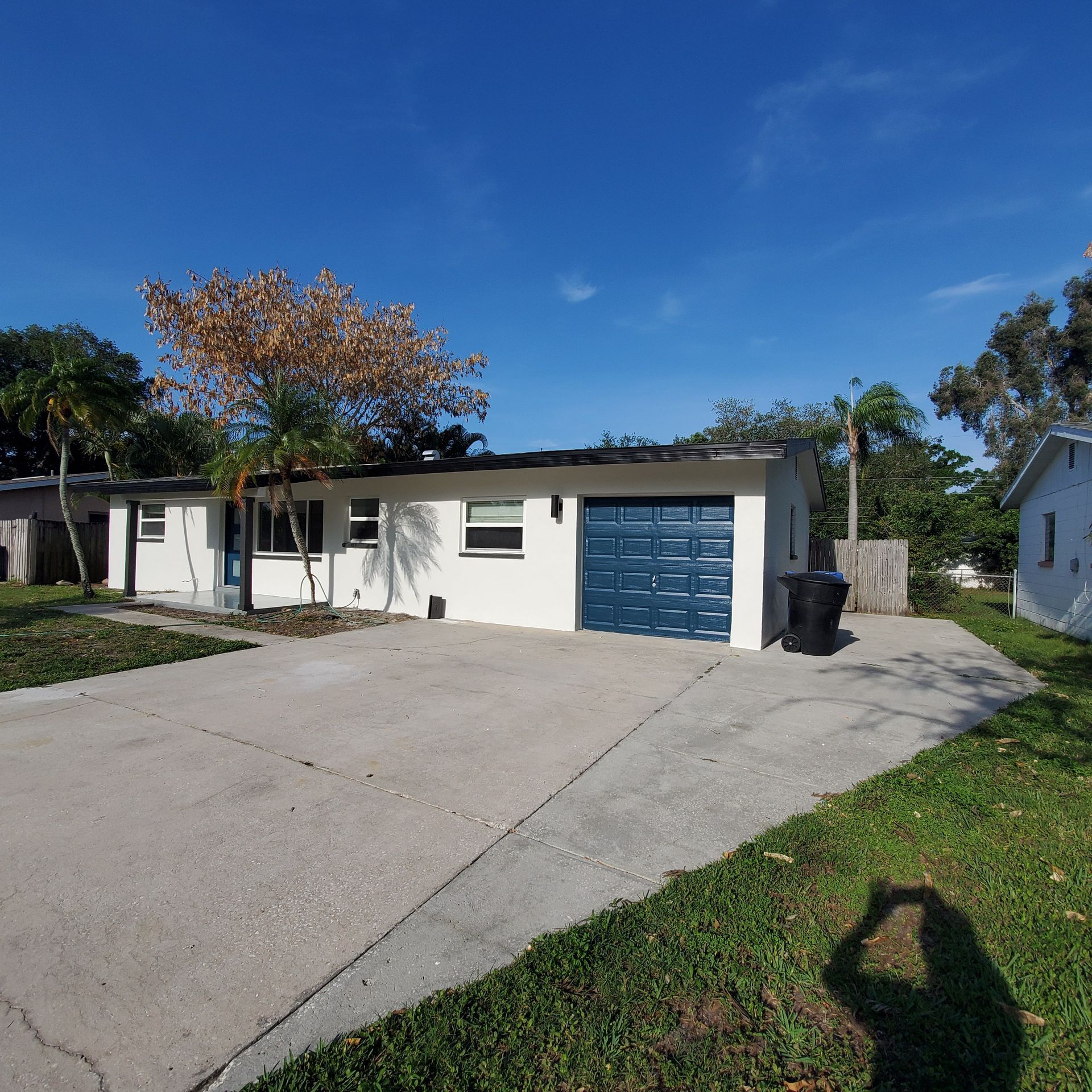 Suburban house with white exterior, blue garage door, driveway, and green lawn under a clear blue sky