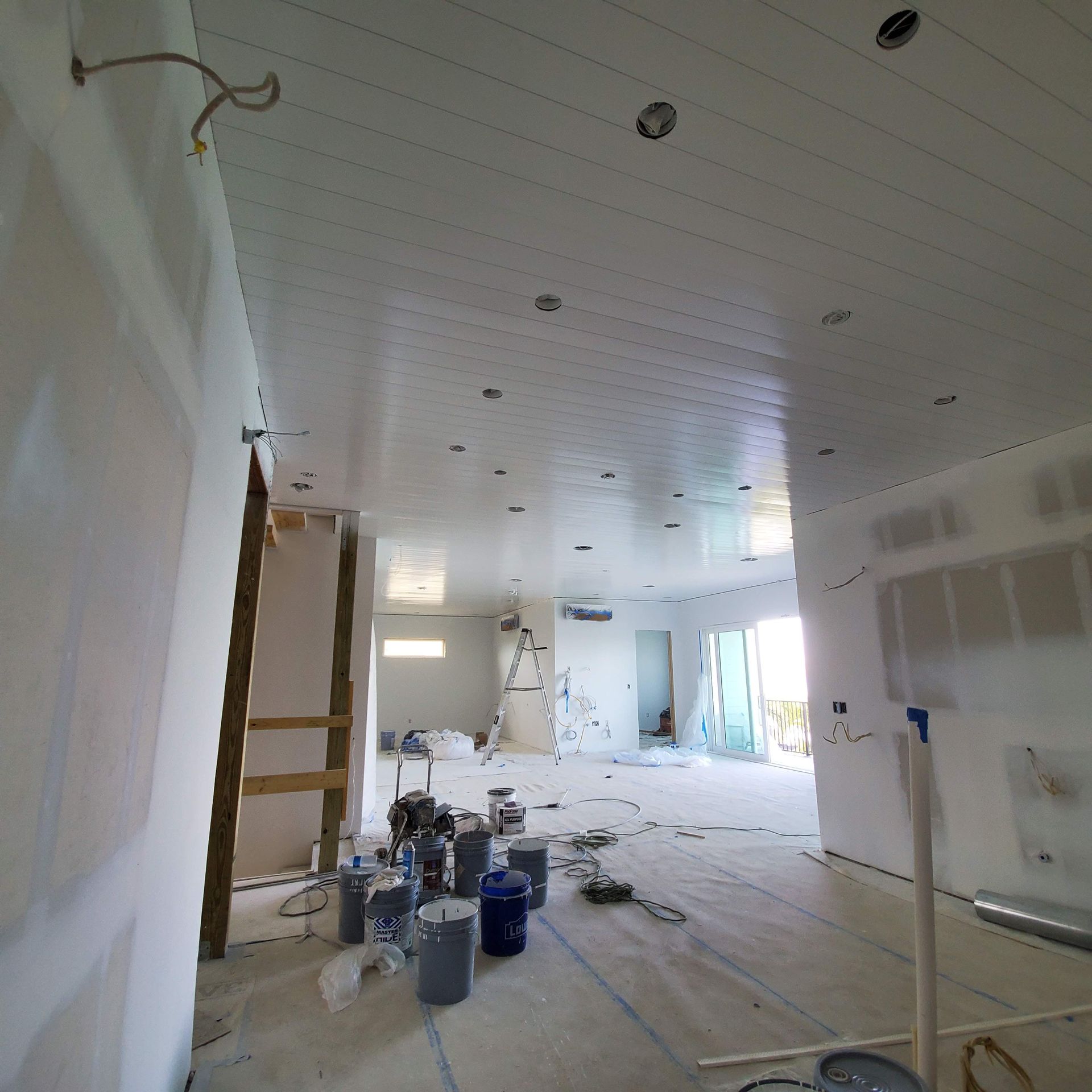 Renovation underway in a white room with unfinished walls, paint supplies, ladders, and debris on the floor