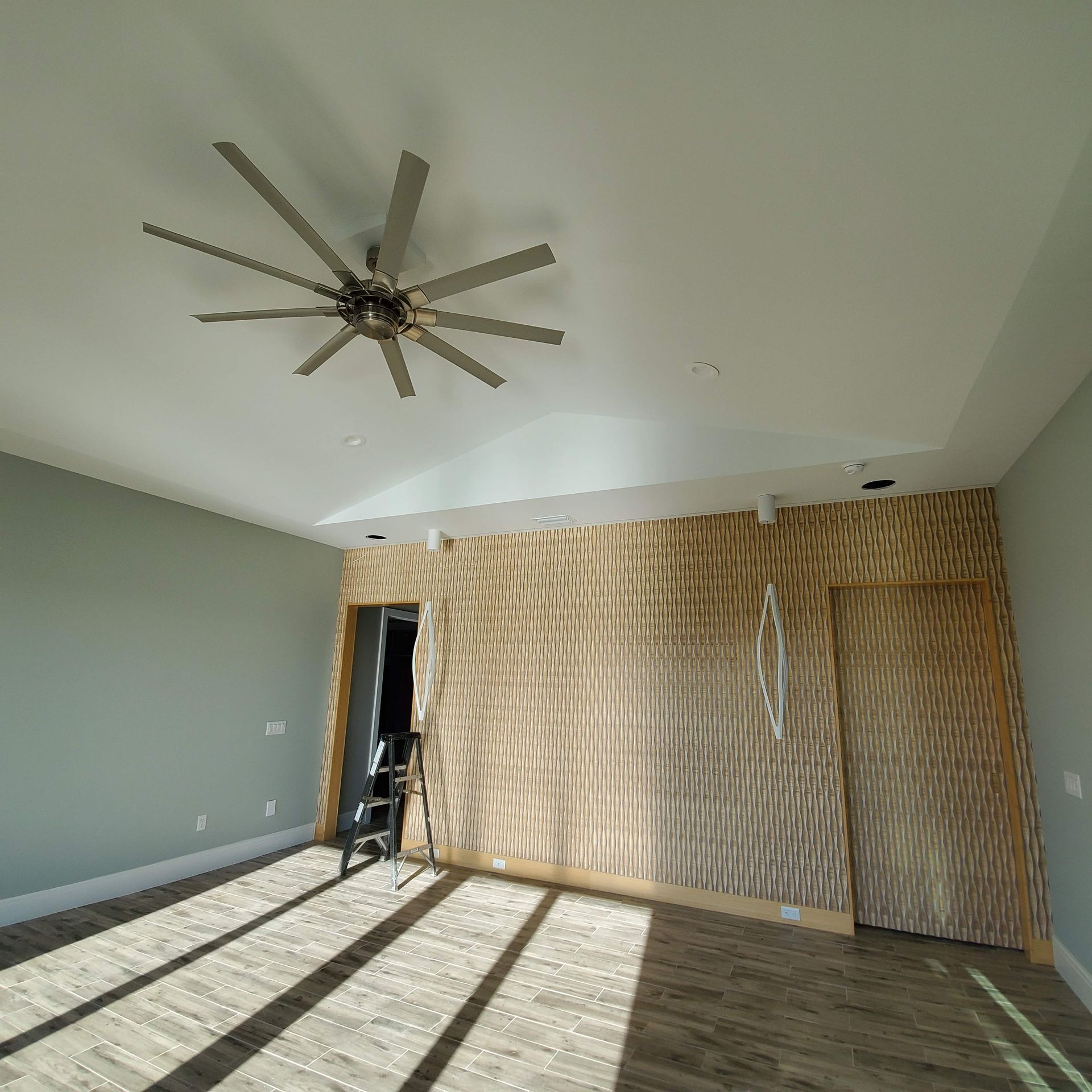 Empty room with a ceiling fan, wood floors, and sunlight casting striped shadows on walls and floor.