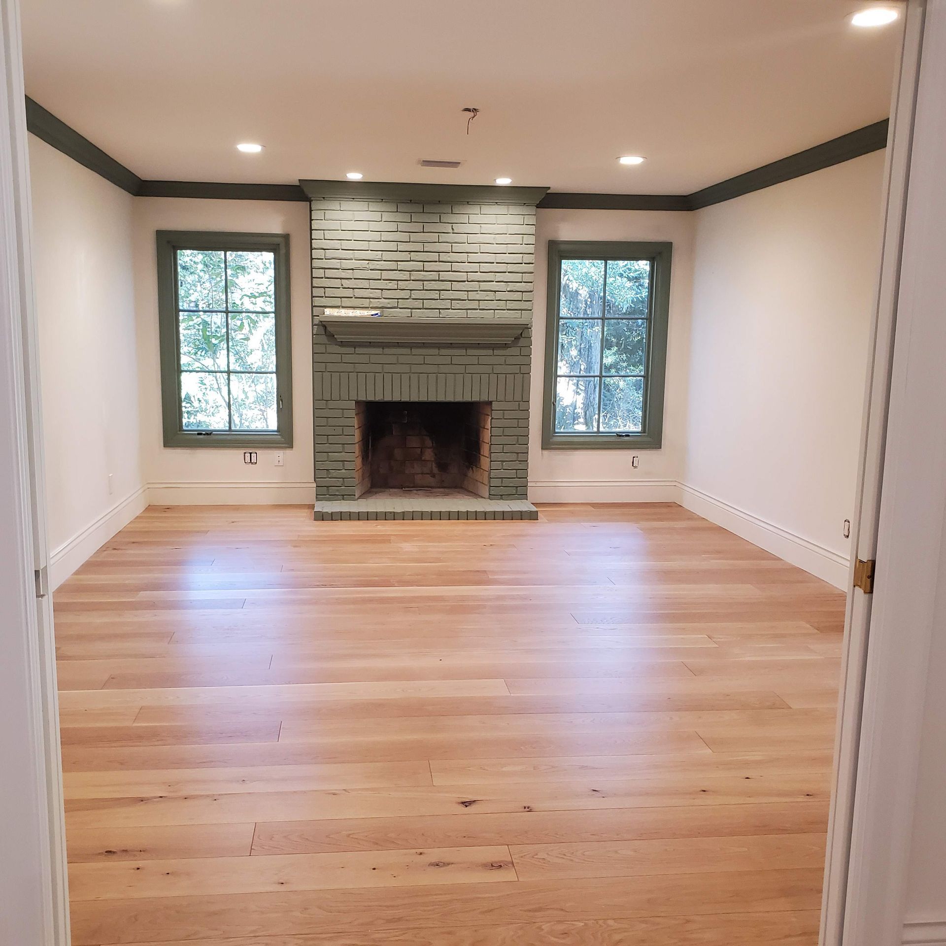 Empty living room with hardwood floors, white walls, and a stone fireplace centered between two windows.