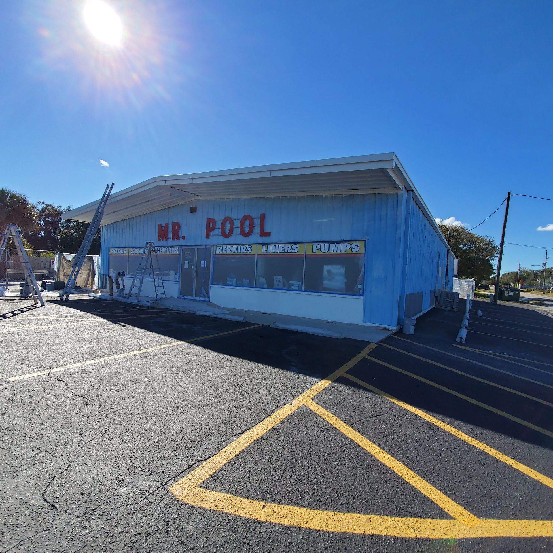 Blue storefront labeled “Mr. Pool” in a sunny parking lot with yellow lines and a clear sky