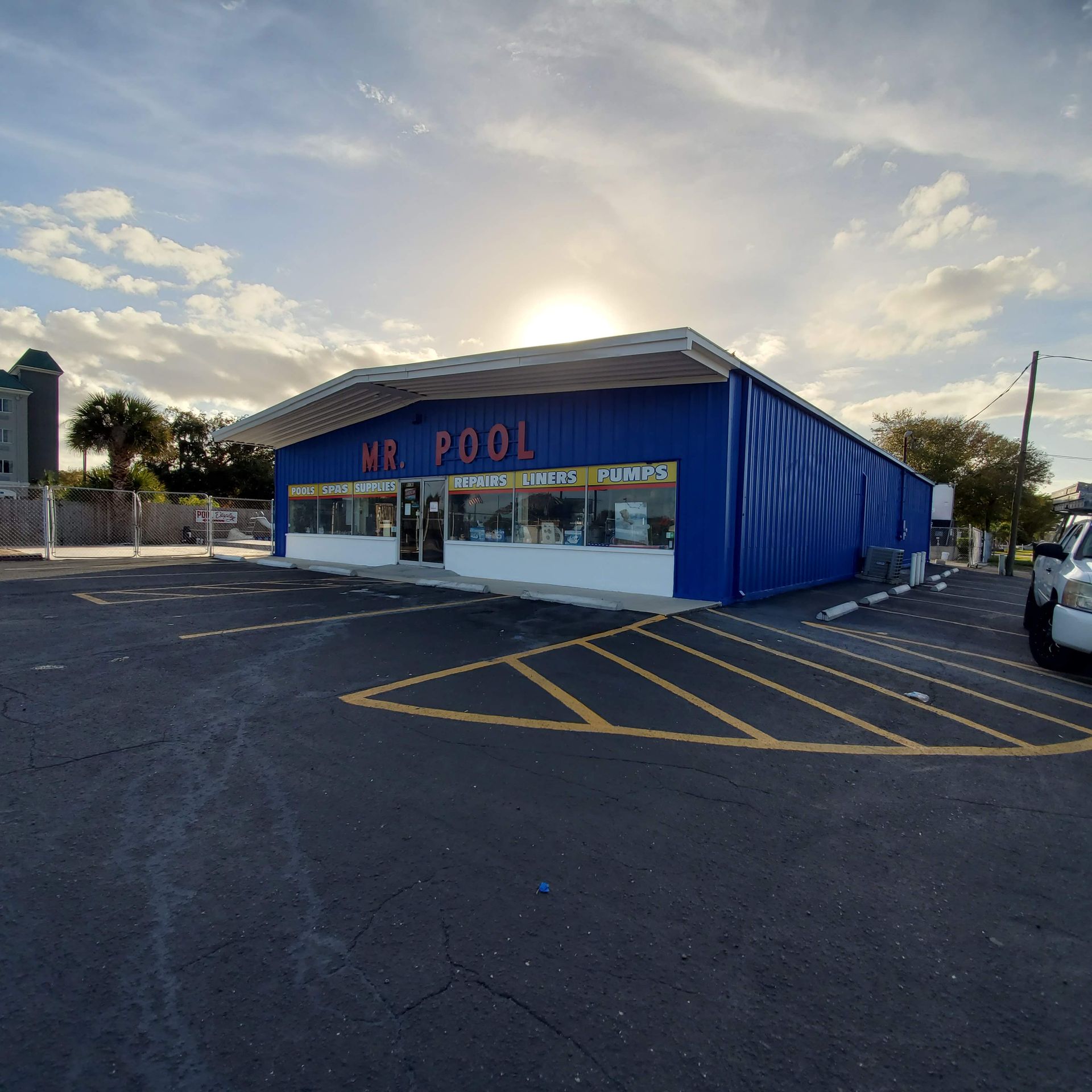 Blue “VR Pool” storefront at sunset, viewed from a parking lot with yellow-striped spaces