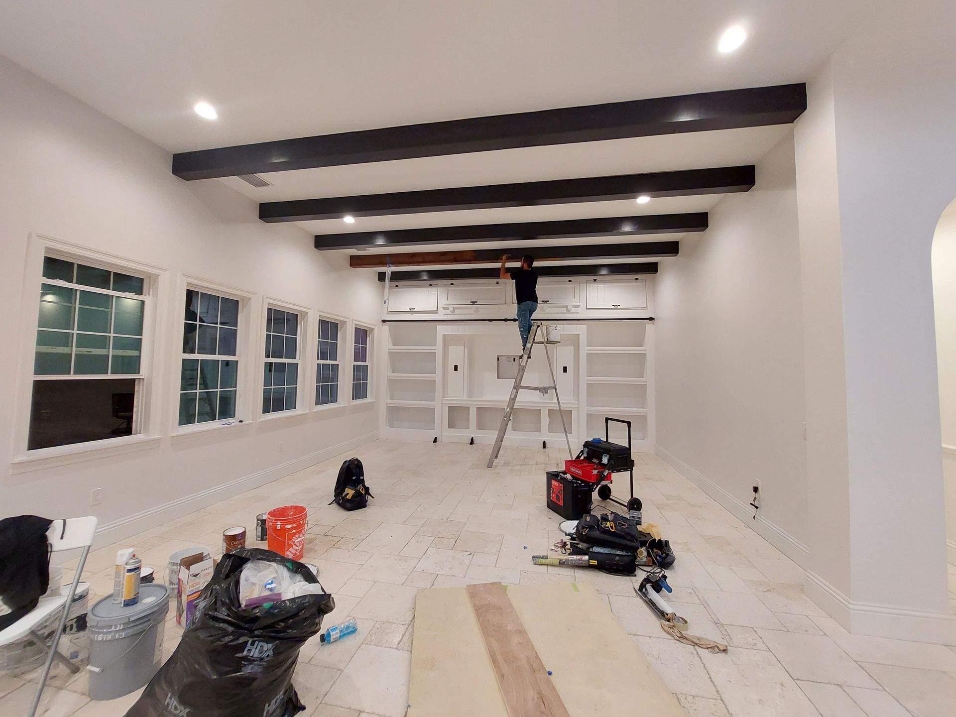 Bright room under renovation with exposed ceiling beams, ladder, tools, and scattered construction materials on the floor