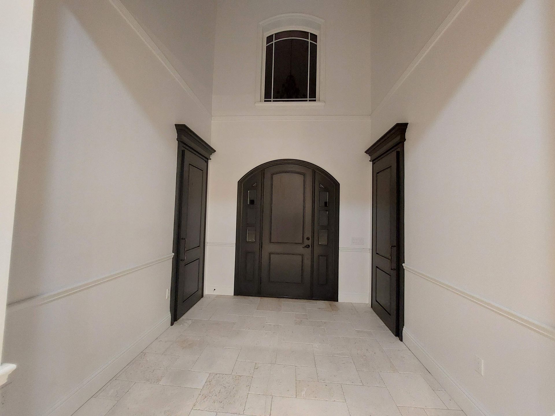 Empty white hallway with dark wooden doors and a high arched ceiling