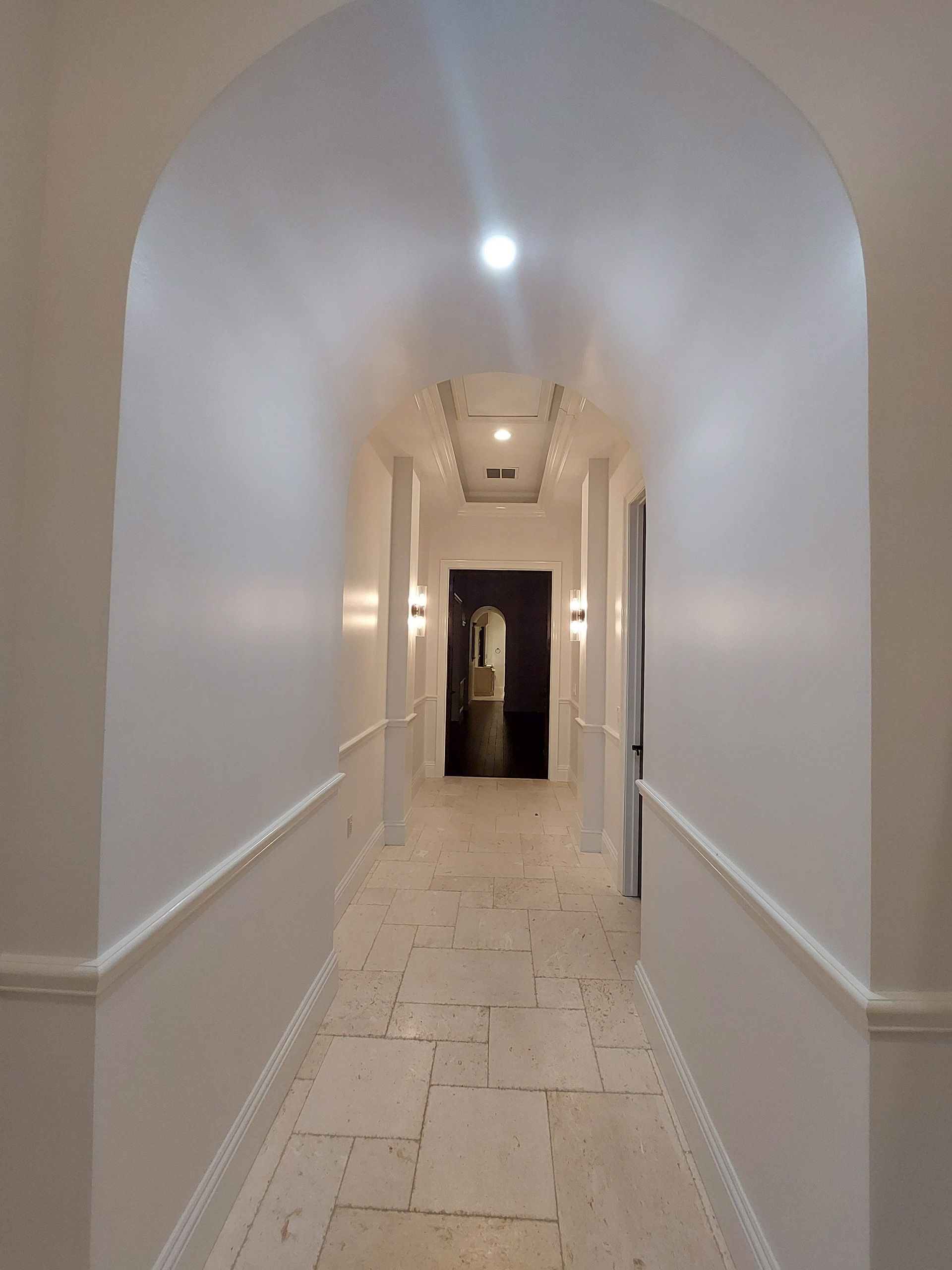 Narrow white hallway with an arched ceiling, tiled floor, and a dark doorway at the far end.
