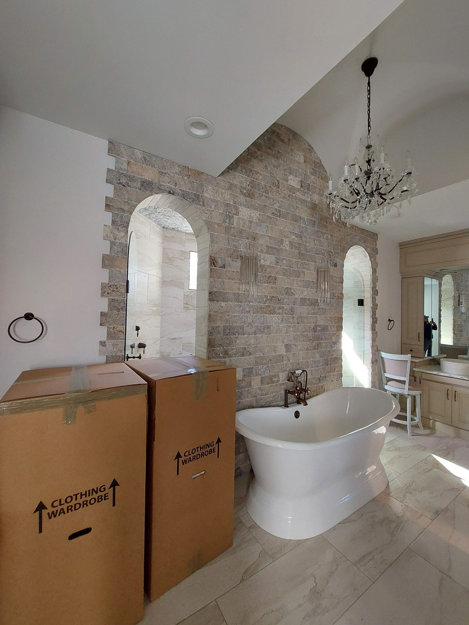 Bathroom with stone accent wall, freestanding tub, chandelier, and cardboard boxes in the foreground