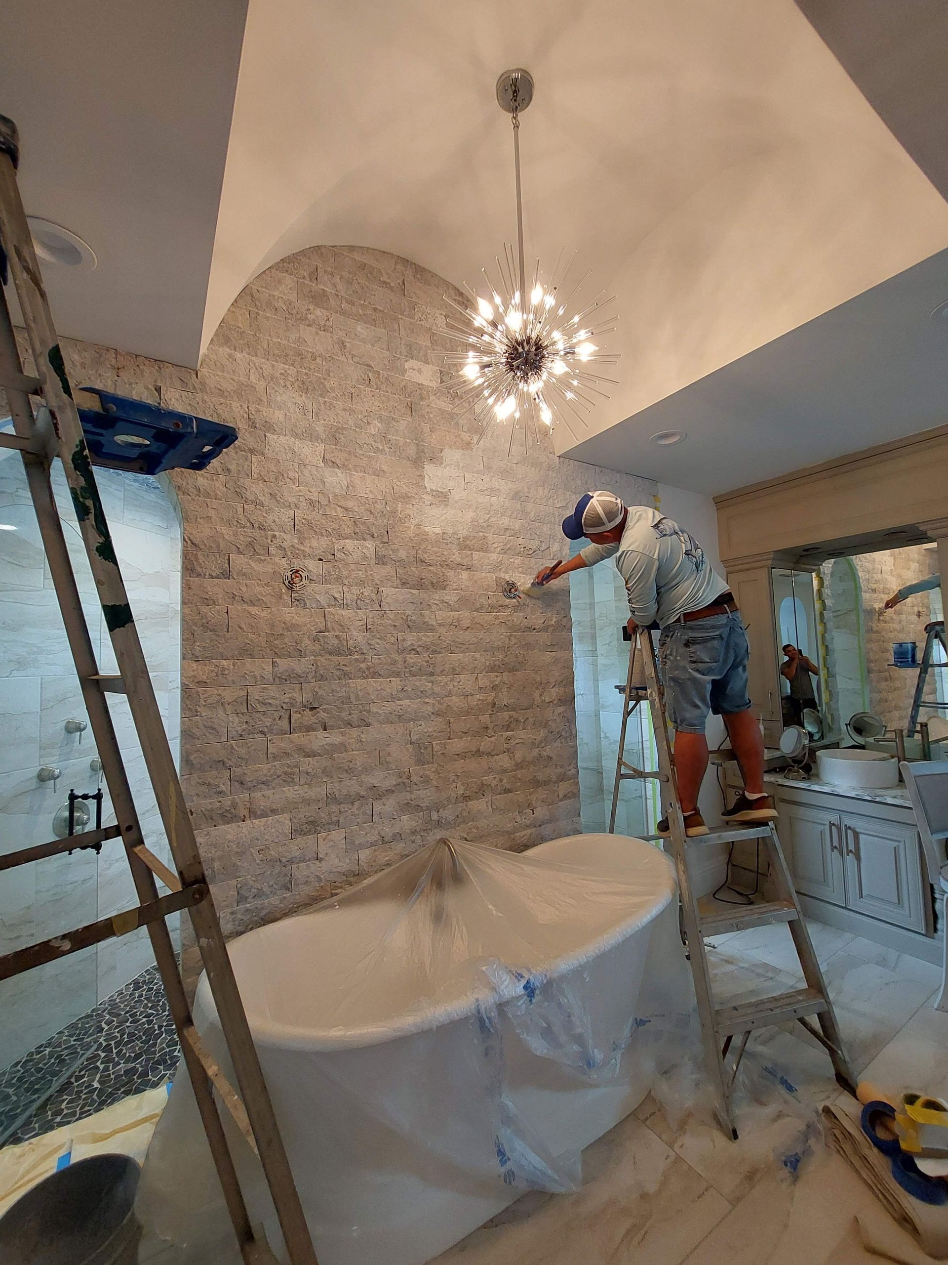 Worker painting a high arched ceiling and brick wall in a room under renovation