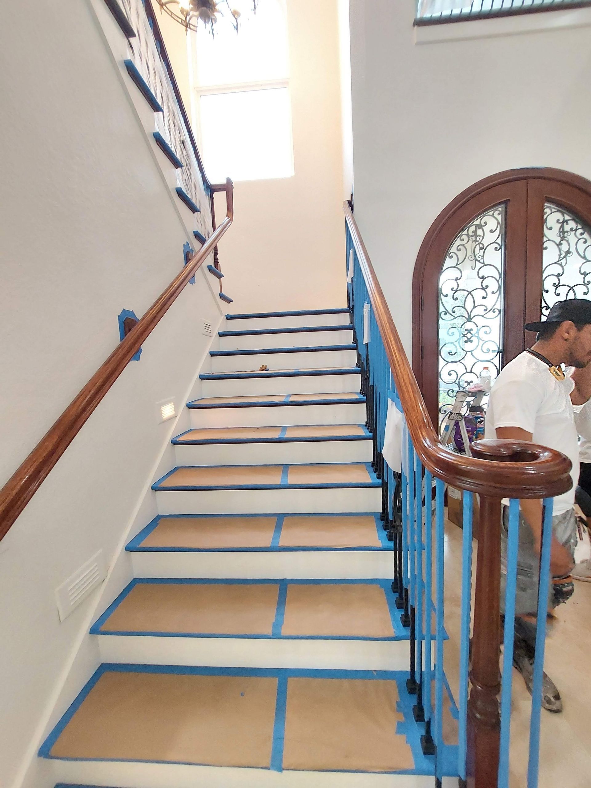 Steep stairway with blue railings and taped steps in a bright indoor hall; a person stands at right.
