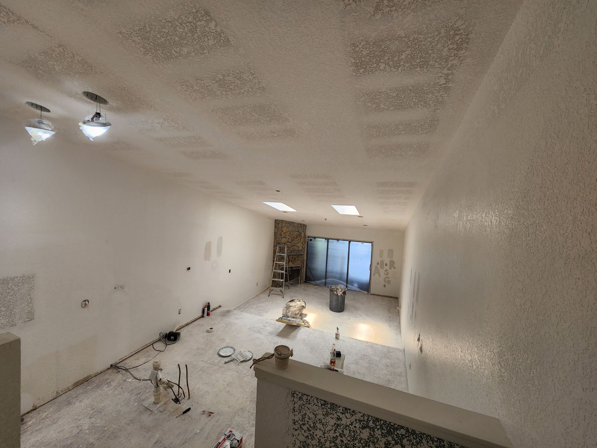 Empty white room under renovation with tools, ceiling lights, and materials on the floor