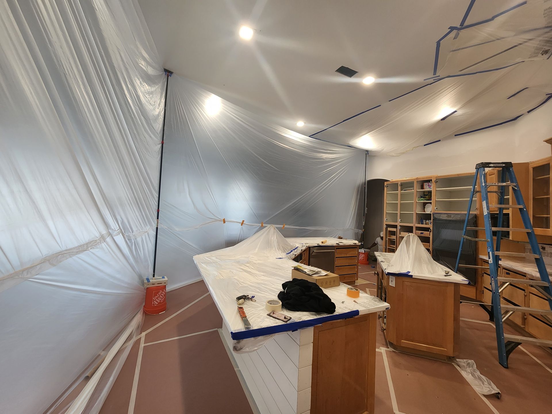 Plastic-covered room under renovation with workbench, ladder, and tools scattered inside.