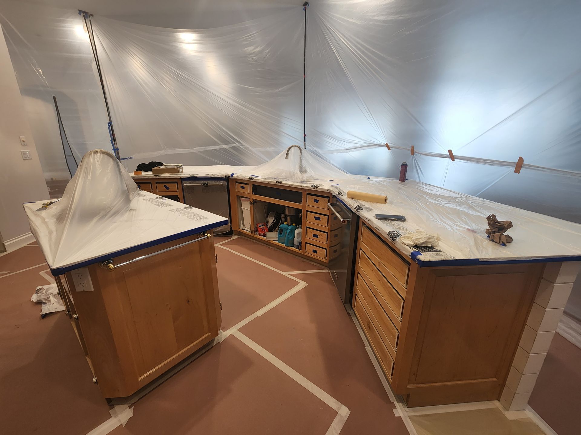 Plastic-covered workshop with wooden cabinets, counters, and tools under construction