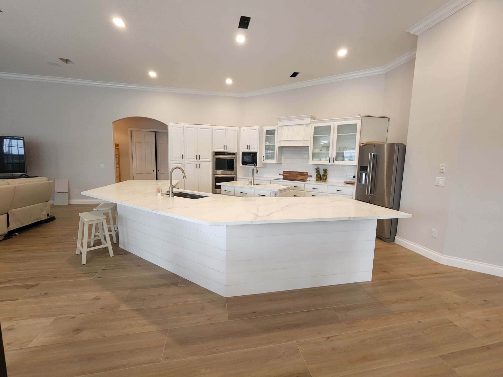 Bright, modern kitchen with a large white island, stainless fridge, and light wood floors