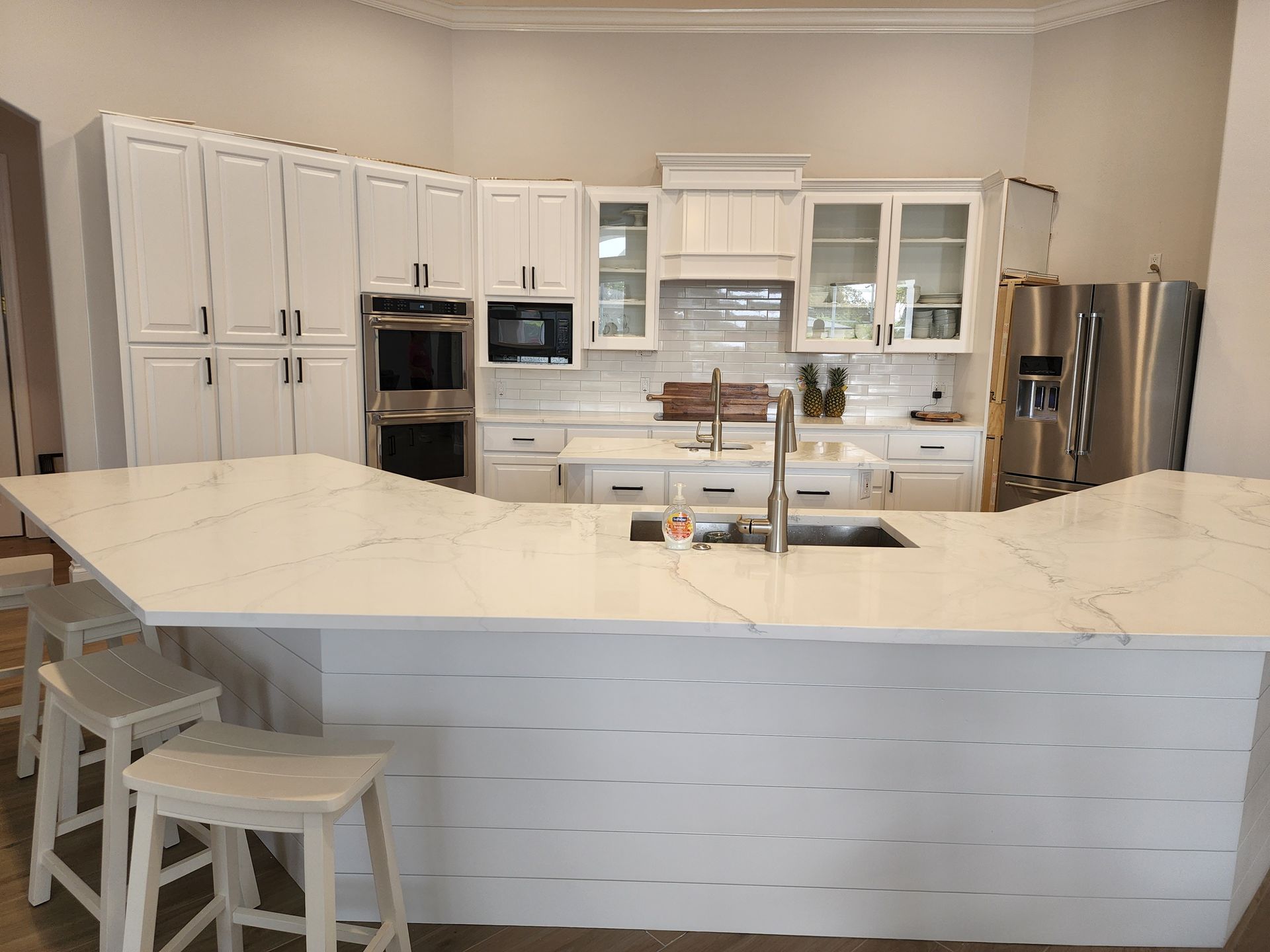 Bright white modern kitchen with large island, stainless appliances, and bar stools