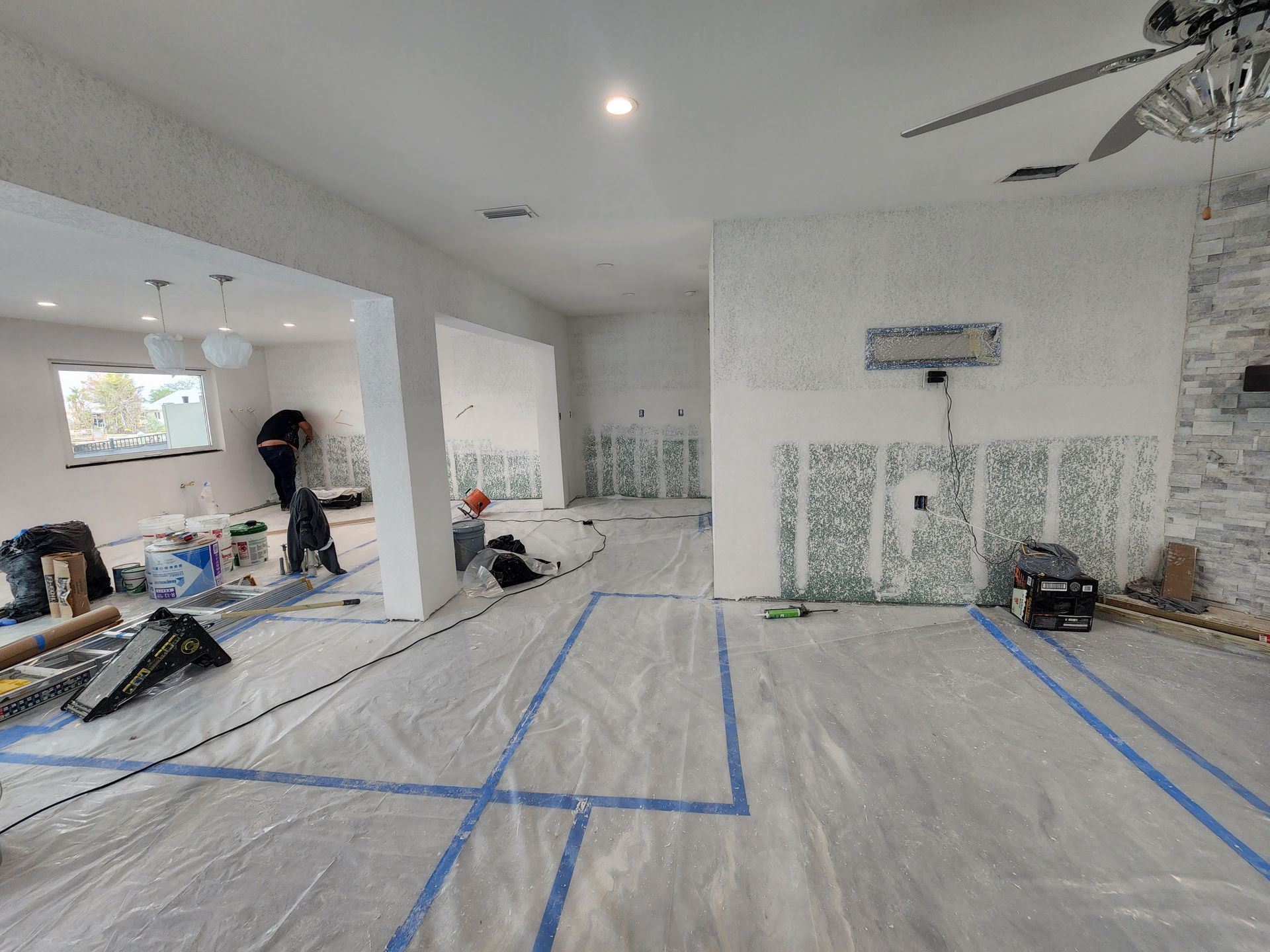 Partially renovated living room with taped plastic-covered floor, white walls, and tools scattered around Partially renovated living room with taped plastic-covered floor, white walls, and tools scattered around