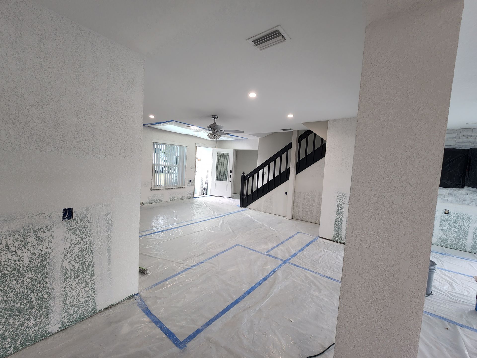 Empty room under renovation with taped-off floor, white walls, and stairs with black railing. Empty room under renovation with taped-off floor, white walls, and stairs with black railing.