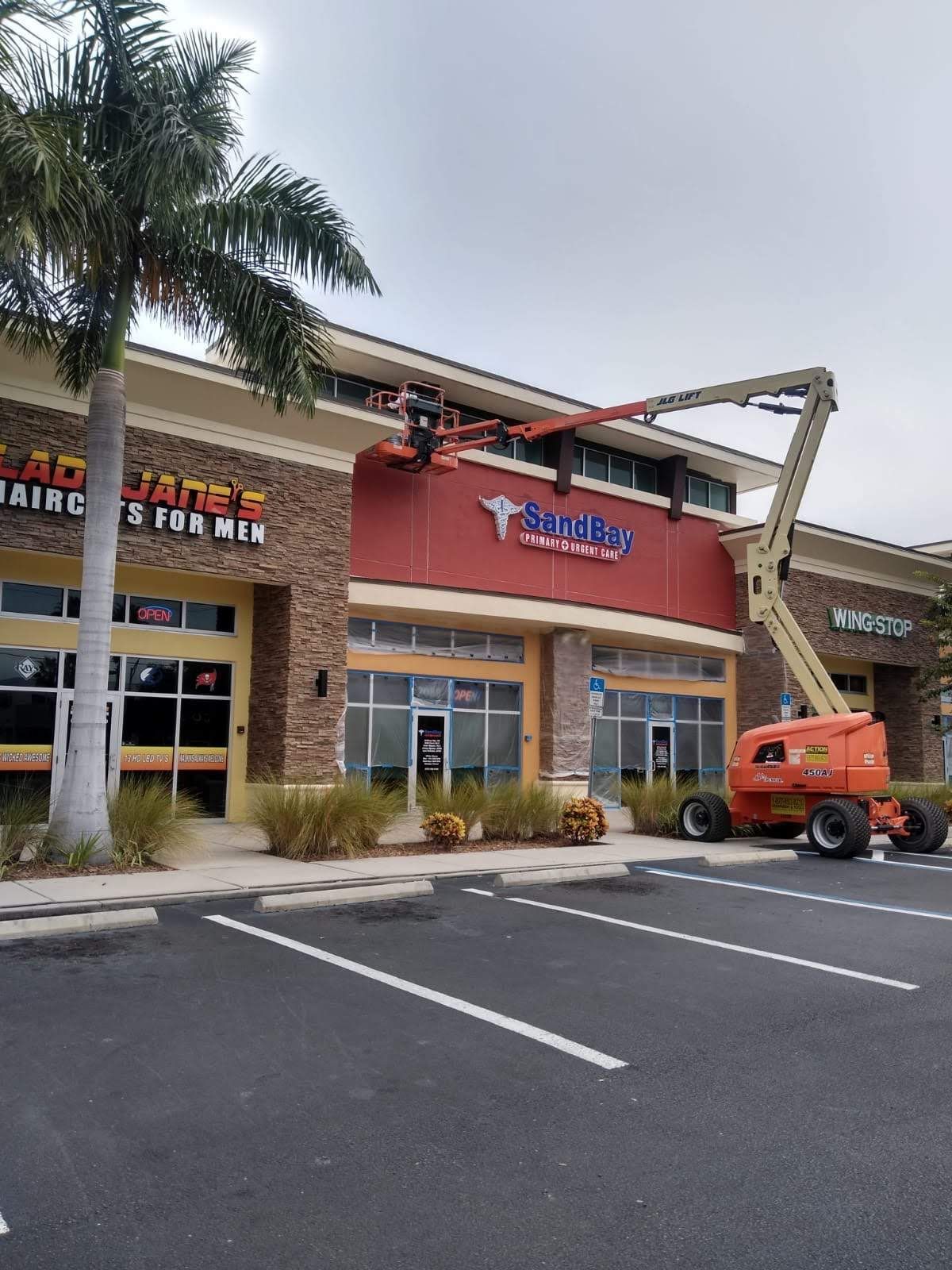 Shopping center storefronts with palm trees and an orange cherry picker parked outside