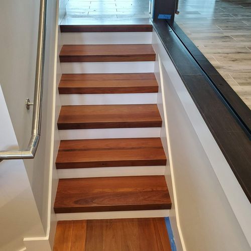 Wooden staircase under construction with white risers and a blue-taped edge at the bottom