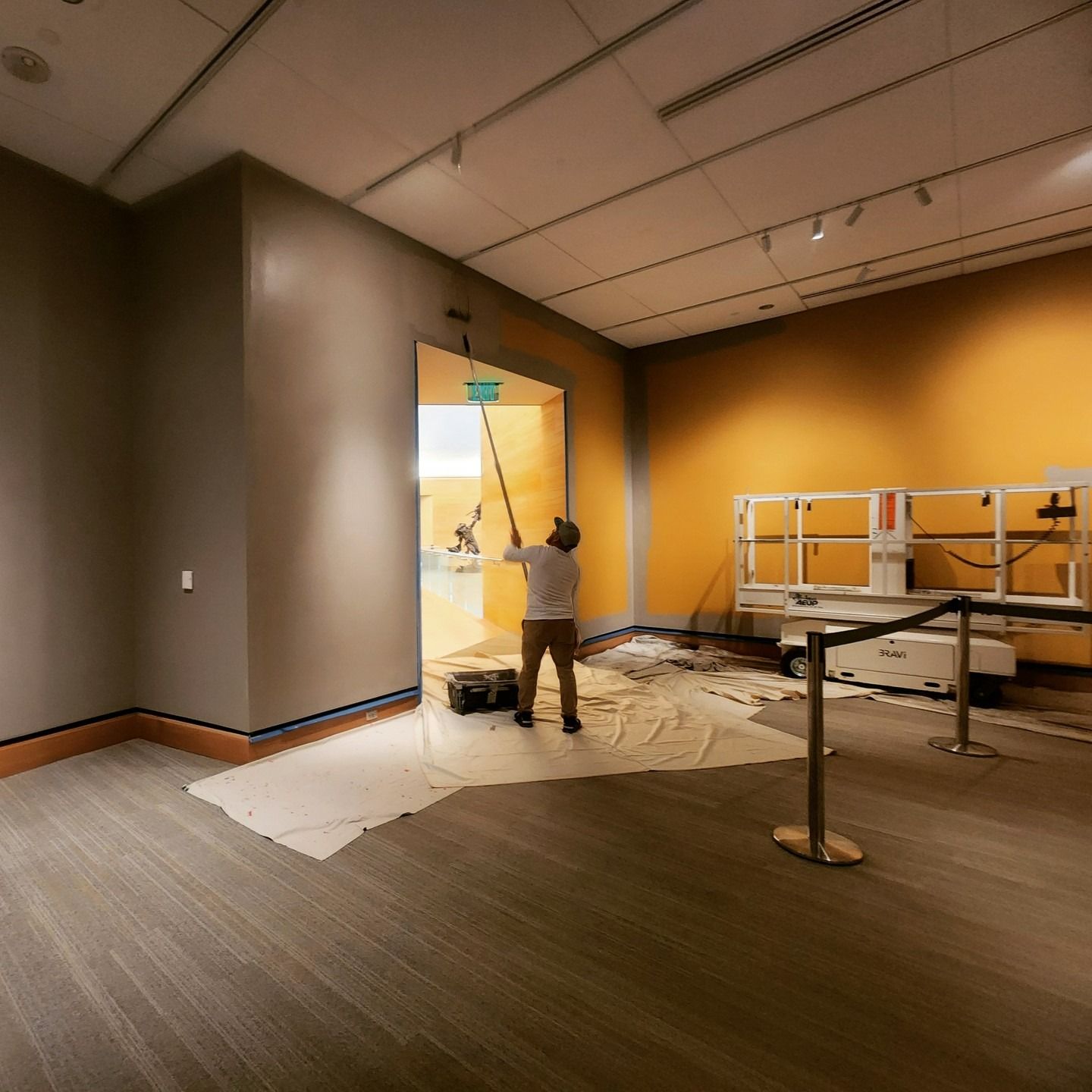 Person painting a doorway in an empty room with orange walls and covered floor.