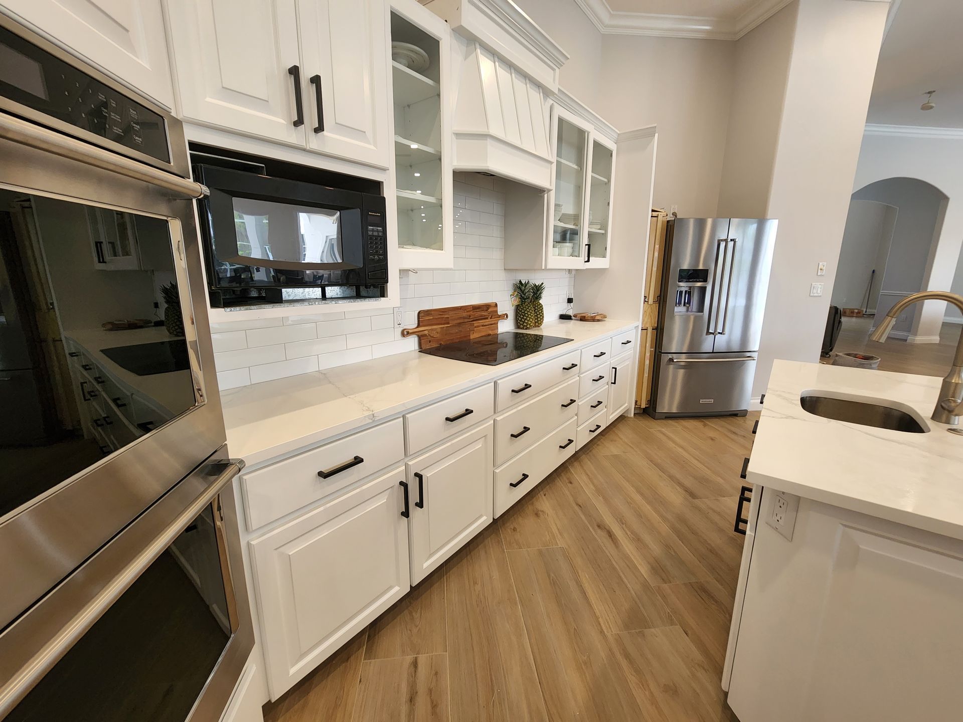 Modern white kitchen with stainless steel appliances, marble countertops, and wood flooring
