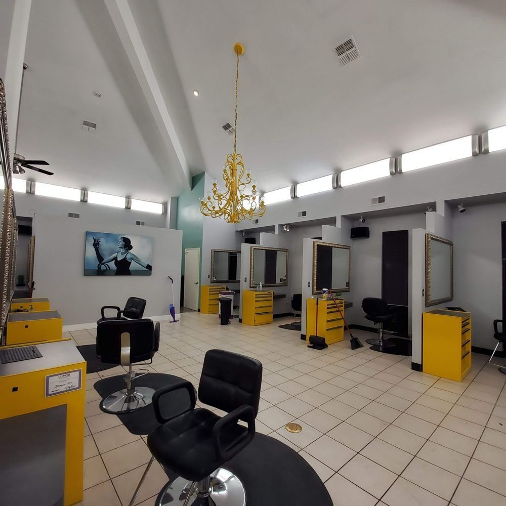 Empty modern salon with black chairs, yellow stations, tiled floor, and a chandelier beneath a white ceiling