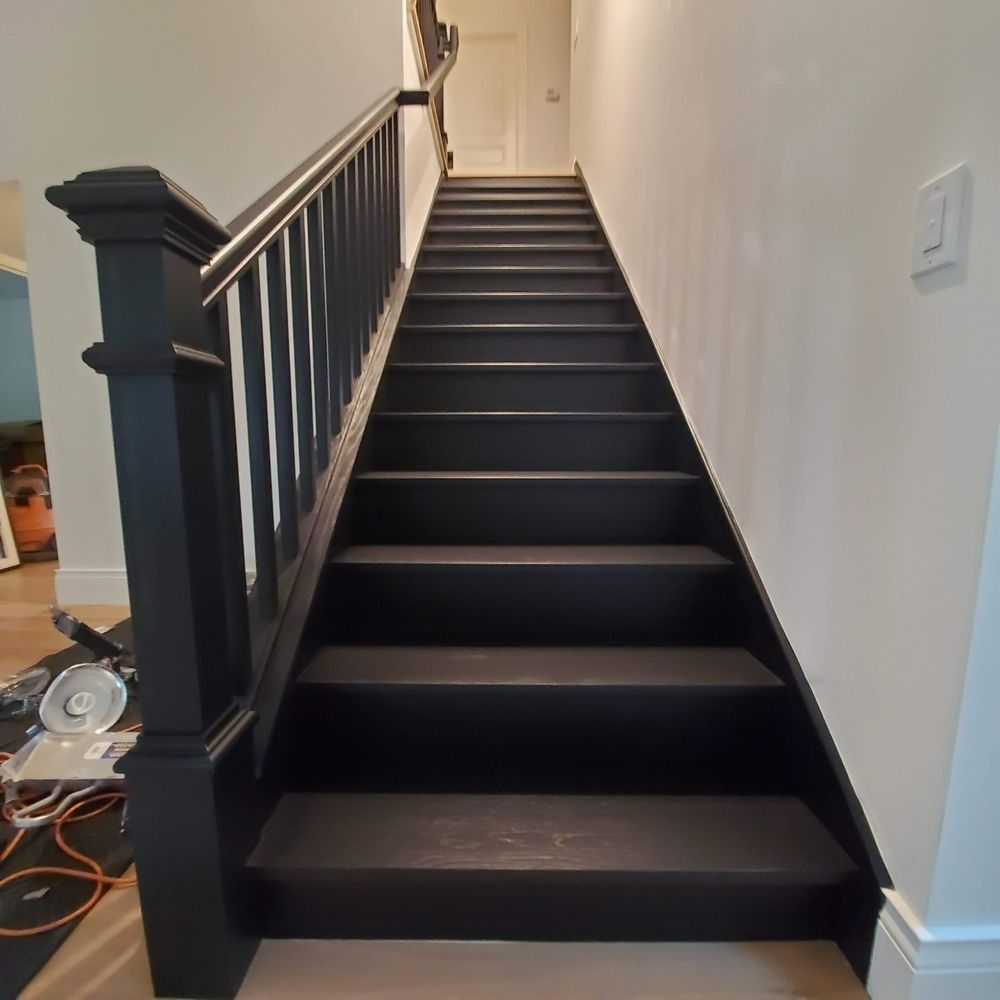 Black staircase with white balusters in a narrow hallway, viewed from the bottom up.